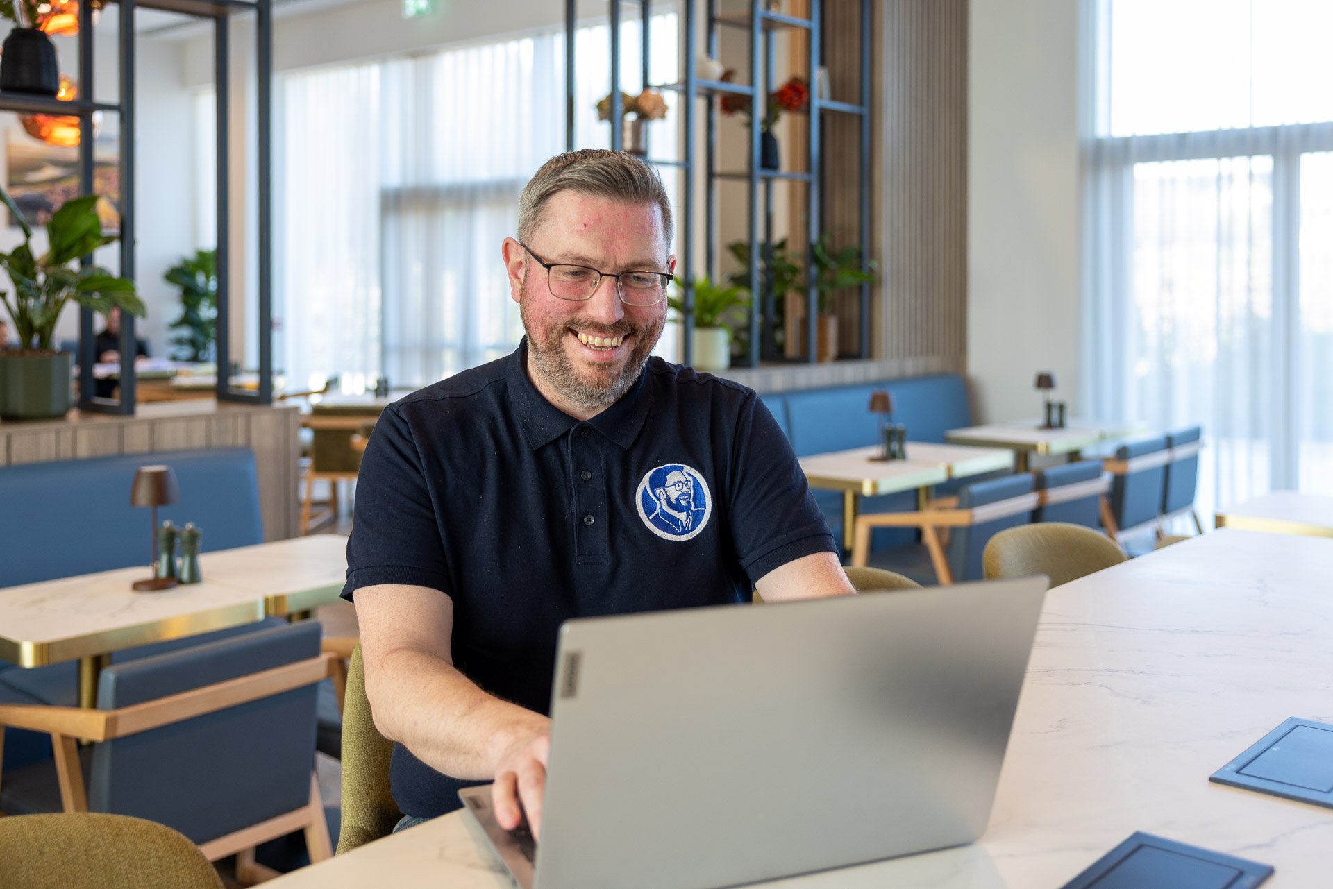 A man with glasses and a beard smiling and talking to a woman with red hair outdoors in a wooded area.