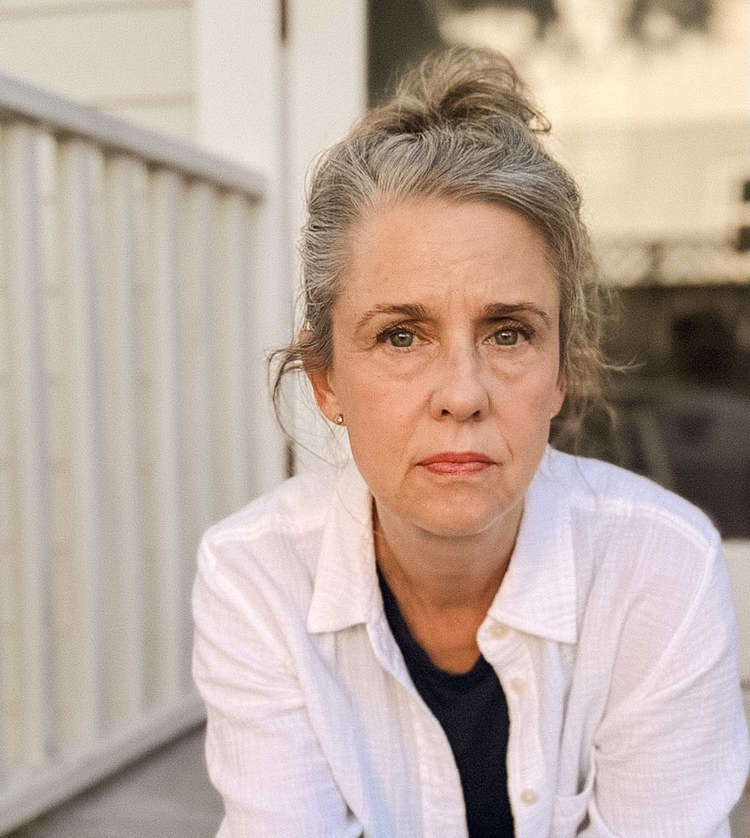 Laura Cantral, wearing a white shirt over a black top, looking directly at the camera with a neutral expression.
