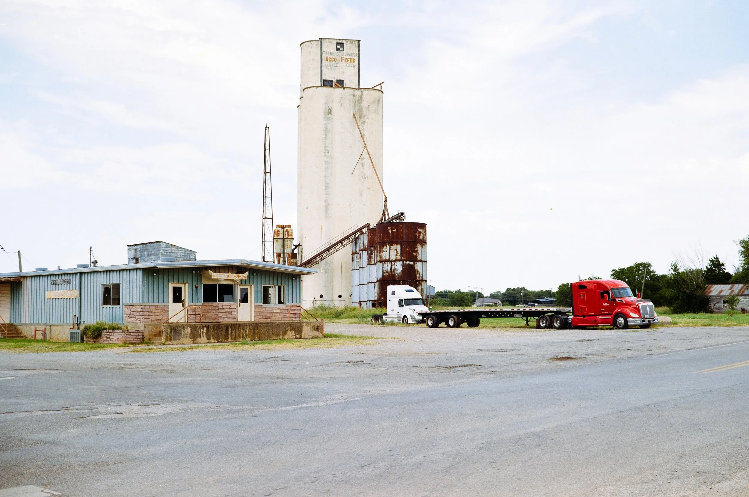Un camion rosso e uno bianco parcheggiati su un piazzale di fronte a un edificio industriale con un silos e strutture arrugginite