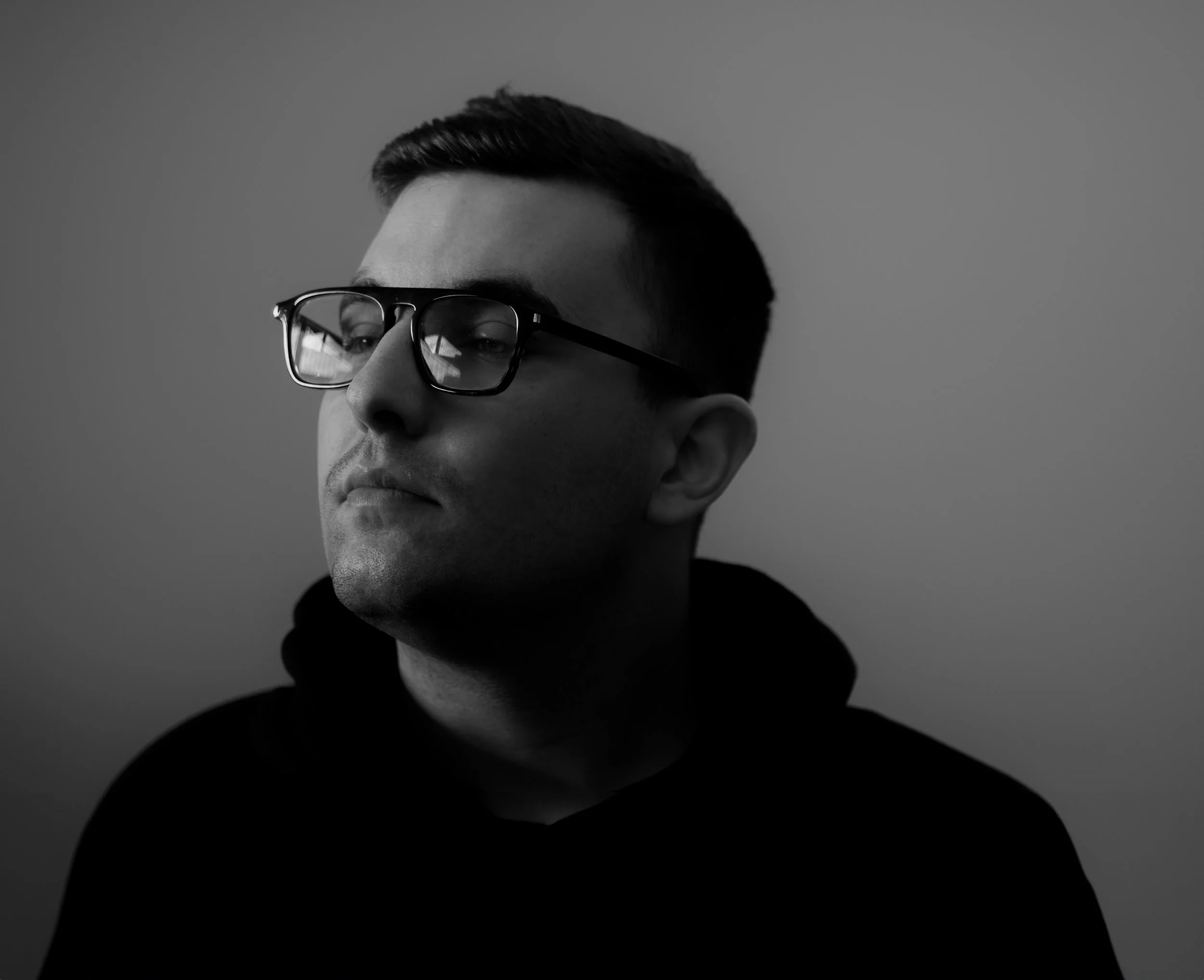 Ritratto in bianco e nero di un giovane uomo con occhiali, sguardo pensieroso, sfondo neutro