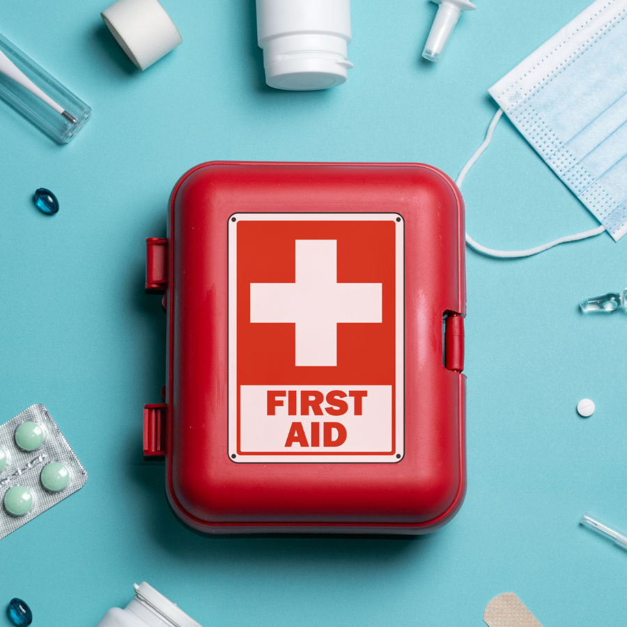Red first aid kit on a blue background surrounded by medical supplies such as pills, a face mask, and bottles.