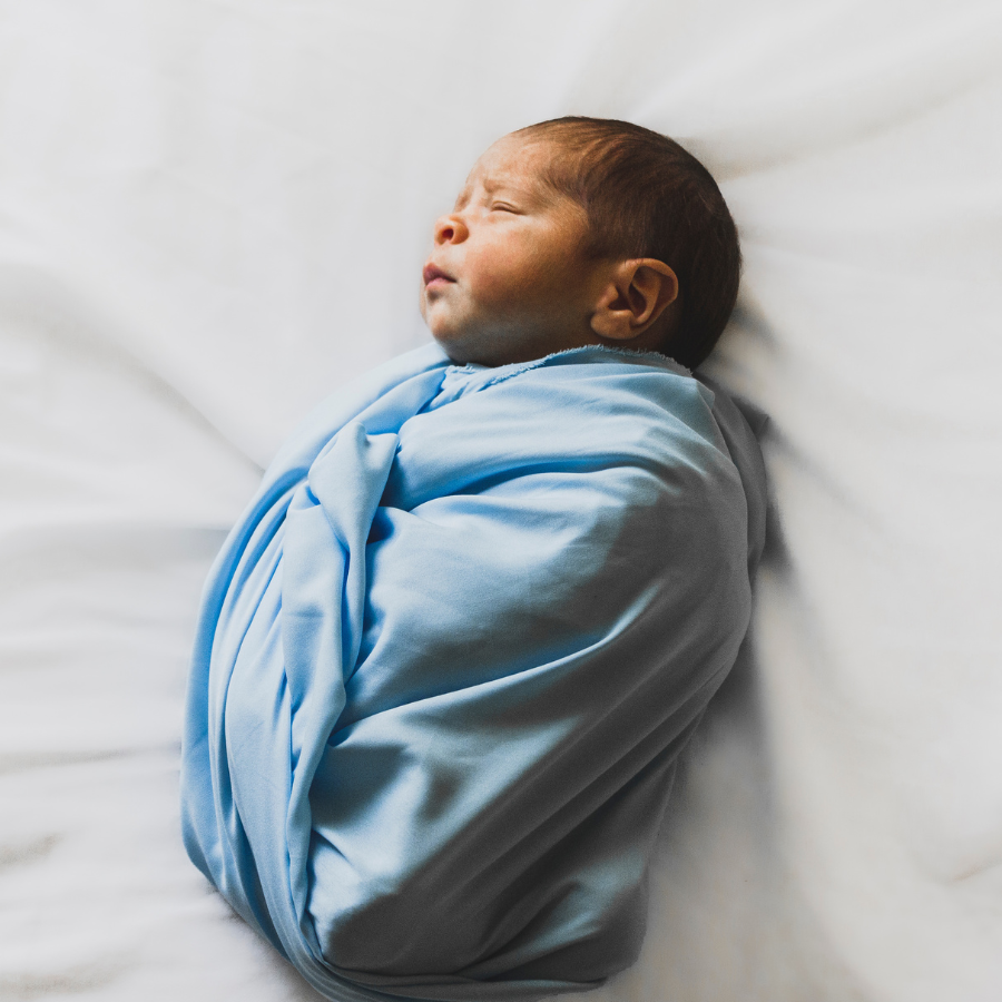 Newborn baby wrapped in a light blue blanket, lying on a white surface, sleeping peacefully.