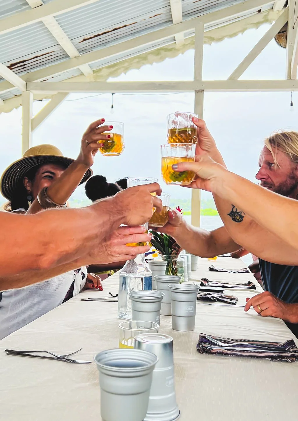 Group of people sitting at a table outdoors, raising glasses of beer in a toast.