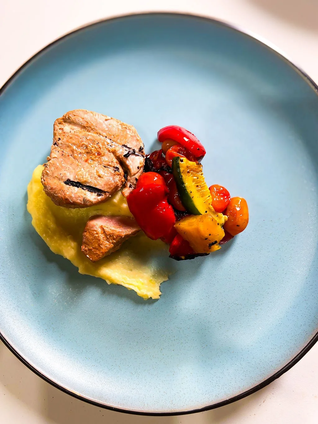 Grilled chicken served on mashed potatoes with a side of roasted vegetables including zucchini, cherry tomatoes, red bell peppers, and yellow squash.