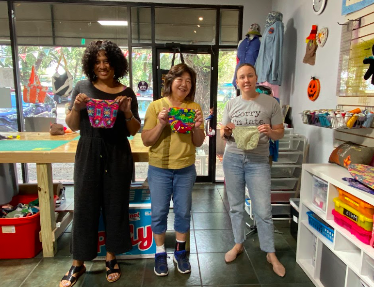 Three smiling people hold up the zipper pouches they made in Sewing 101 Part 3