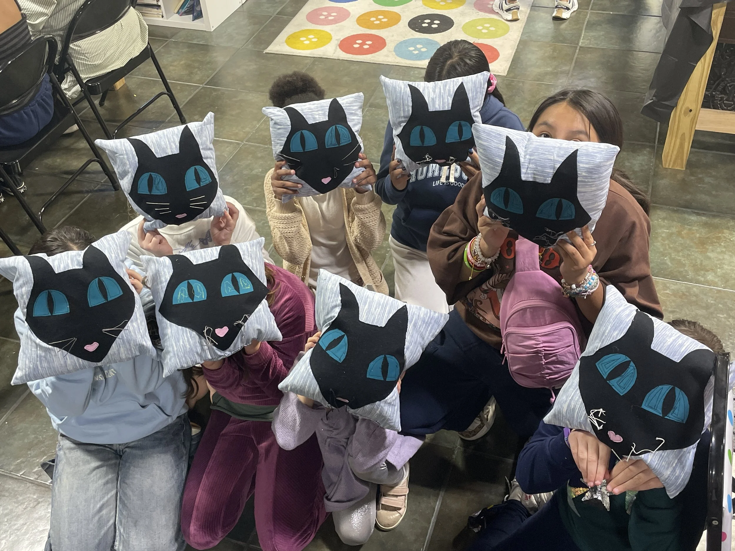 Children hold up pillows with the face of the cat from "Coraline" sewn on