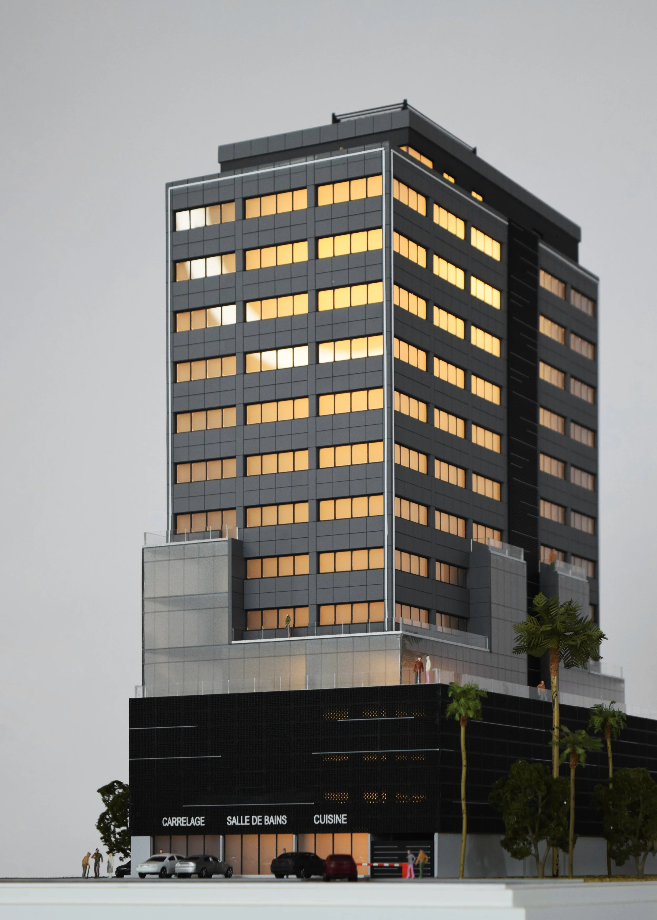 Model of a modern high-rise building with black and gray exterior, illuminated windows, and commercial space on the ground floor with signage for tile, bathroom, and kitchen services, and palm trees around the base.