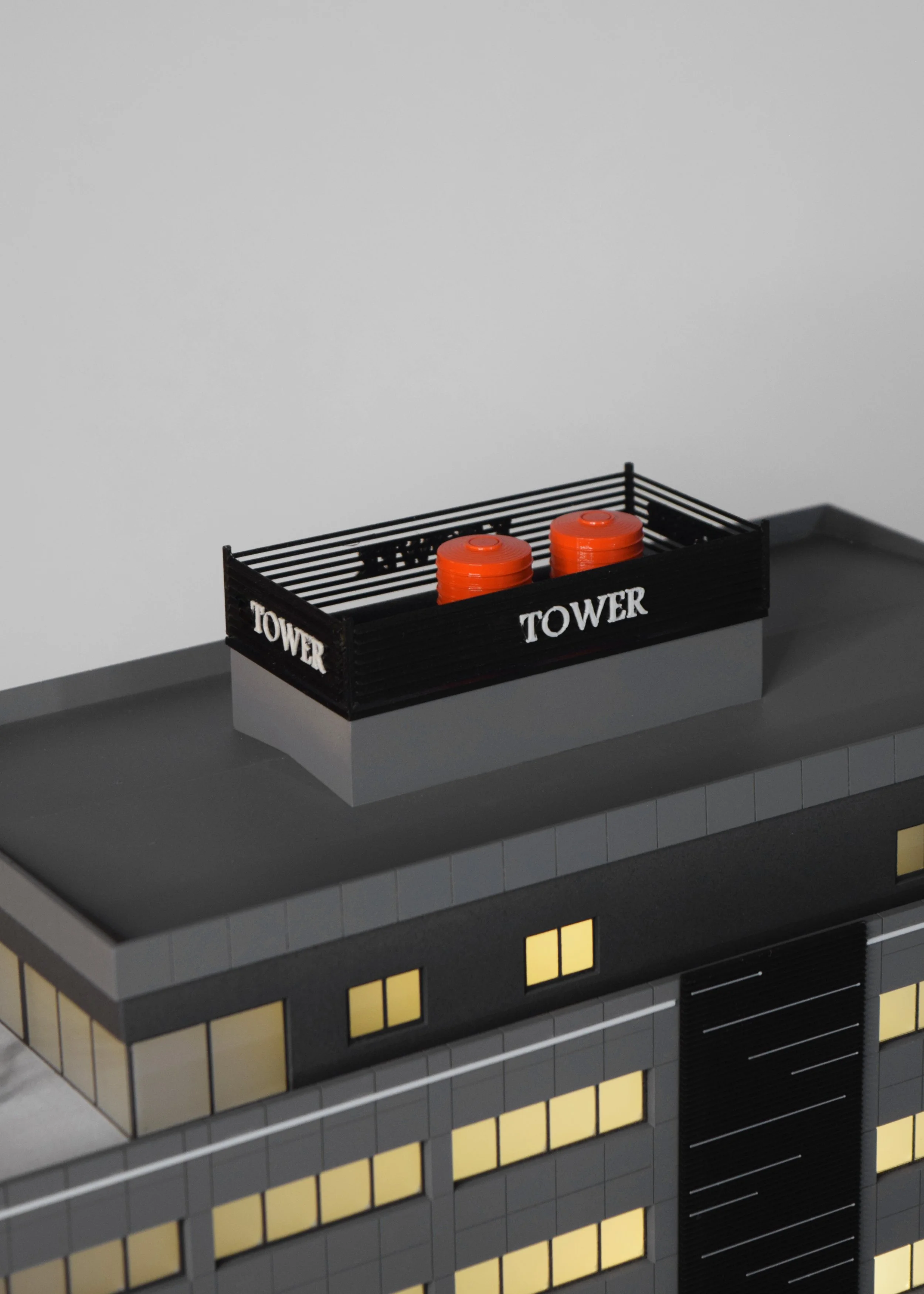 A LEGO replica of a building rooftop with a black railing labeled 'TOWER' and two orange vents on top.