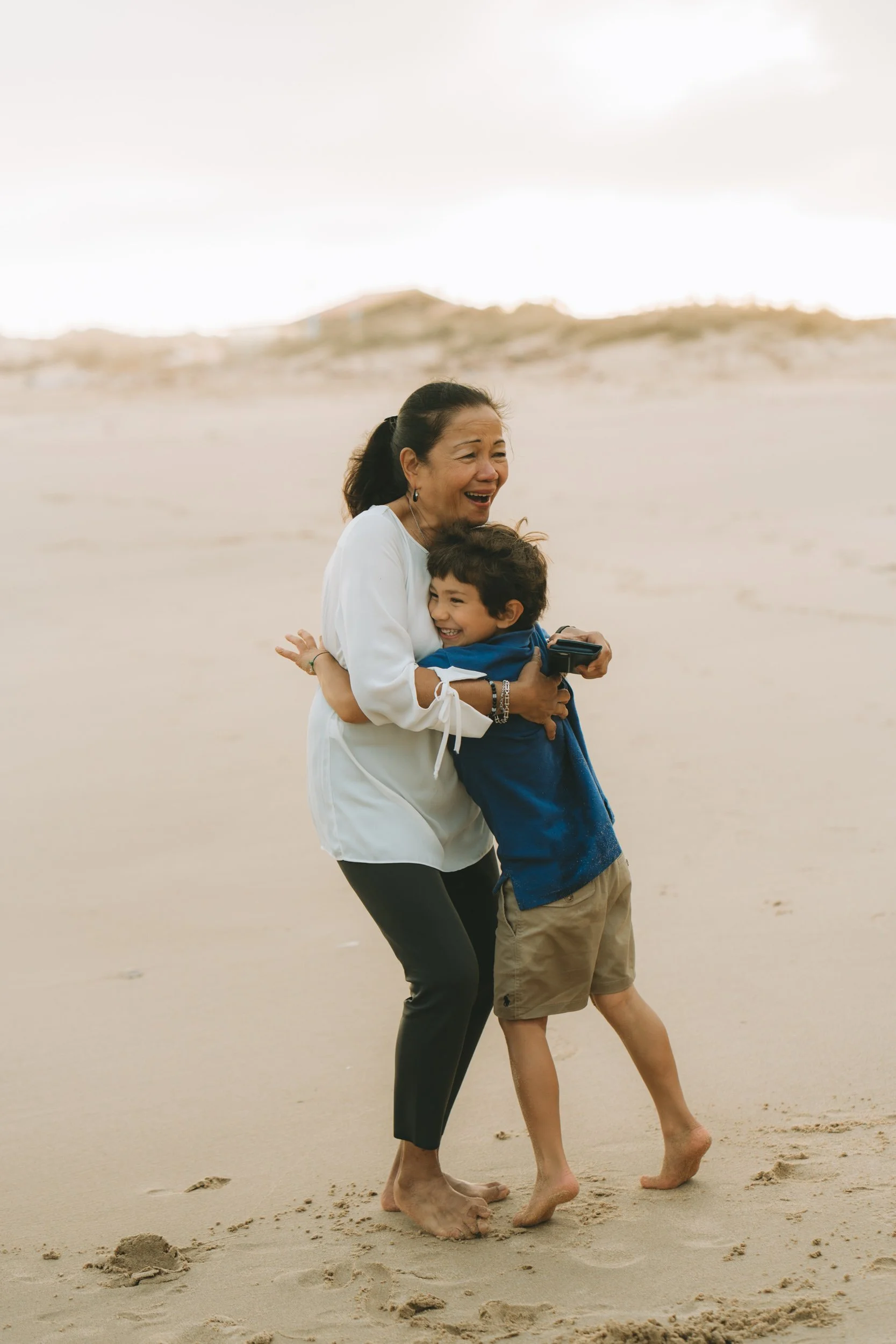 A spontaneous hug between grandmother and child, capturing a real, emotional moment during a family photoshoot at Martinhal beach.