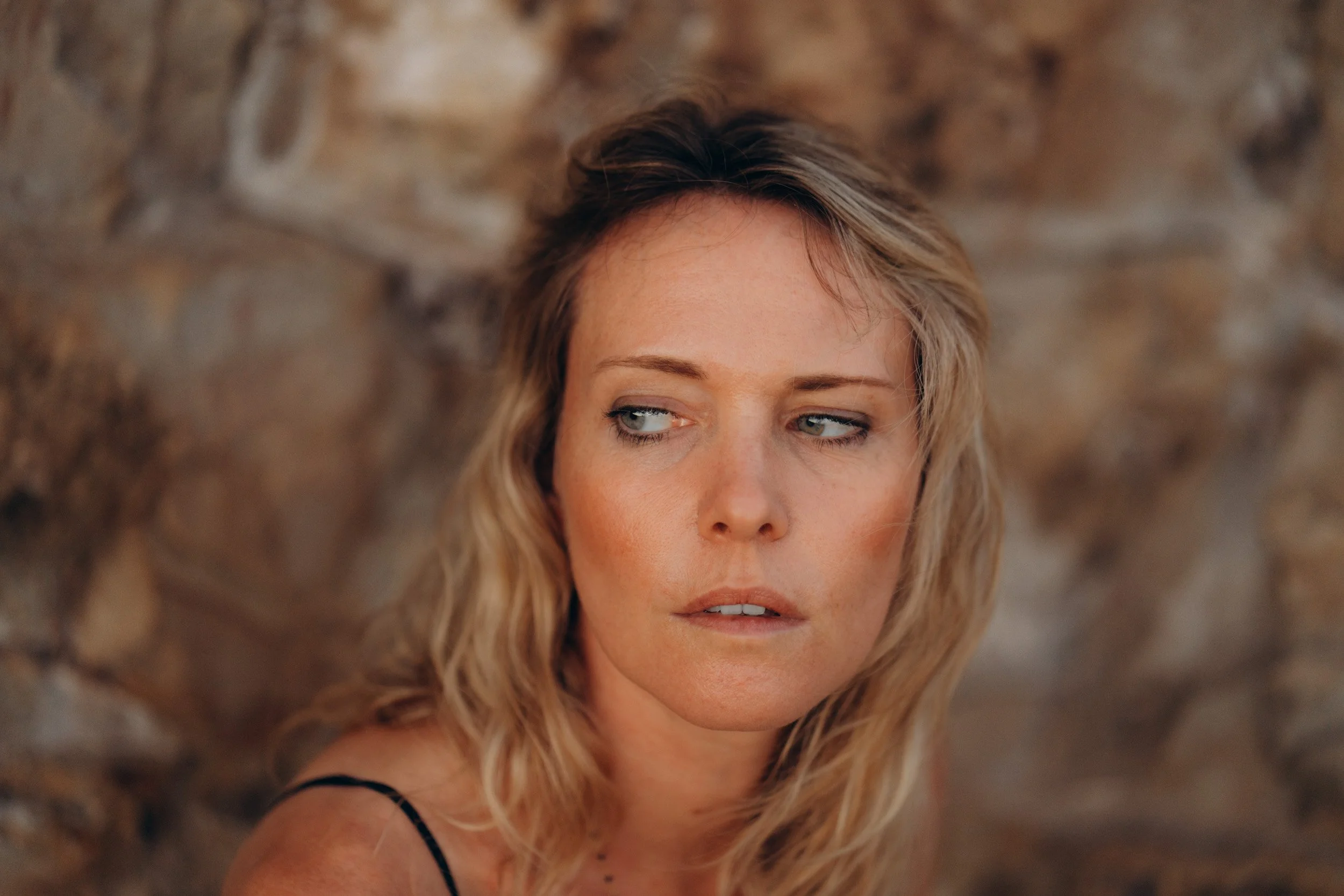 Close-up emotional portrait against textured rock — natural skin tones and soft light Sagres