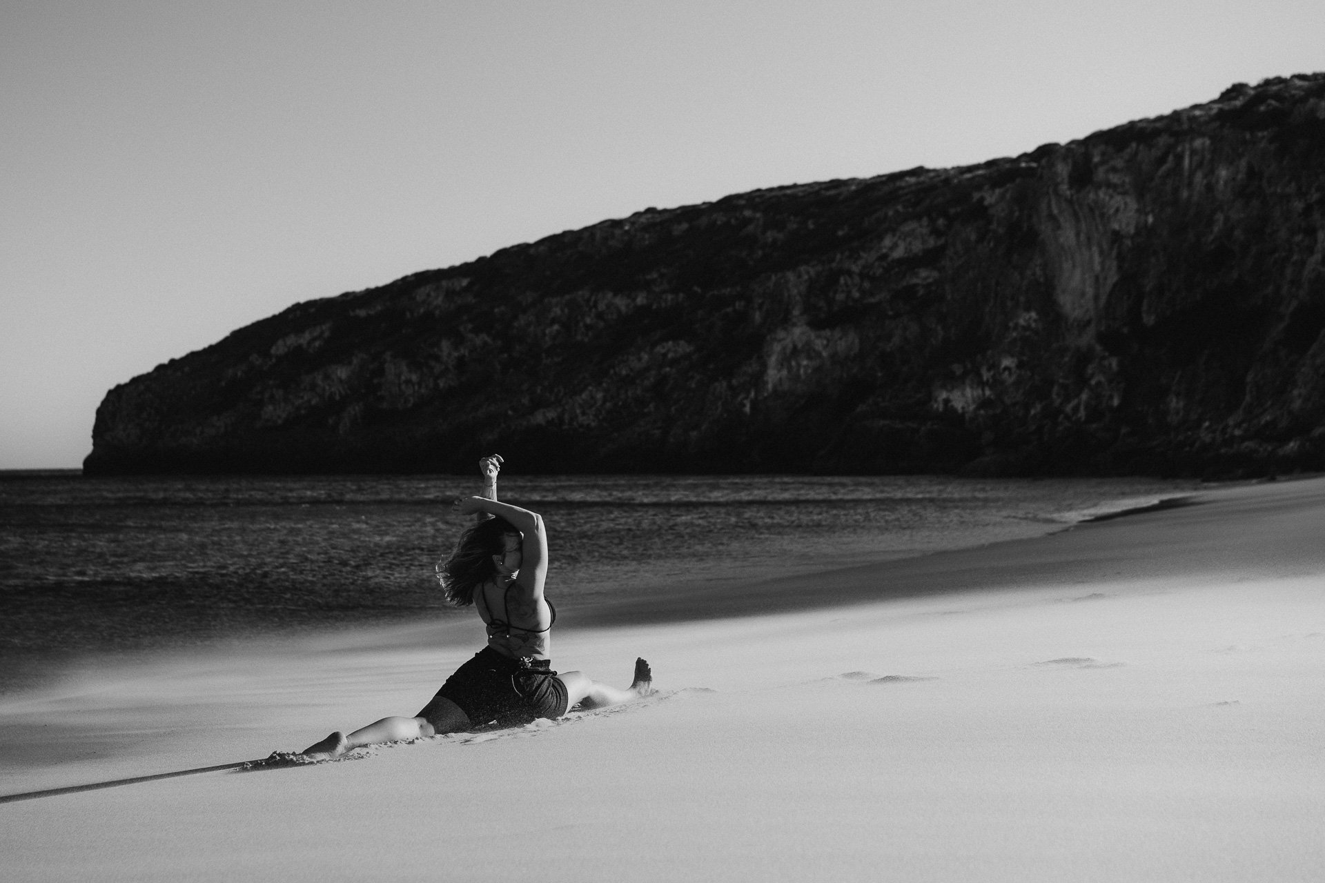 Grounded yoga movement in the sand, with the ocean creating a calm and open backdrop.