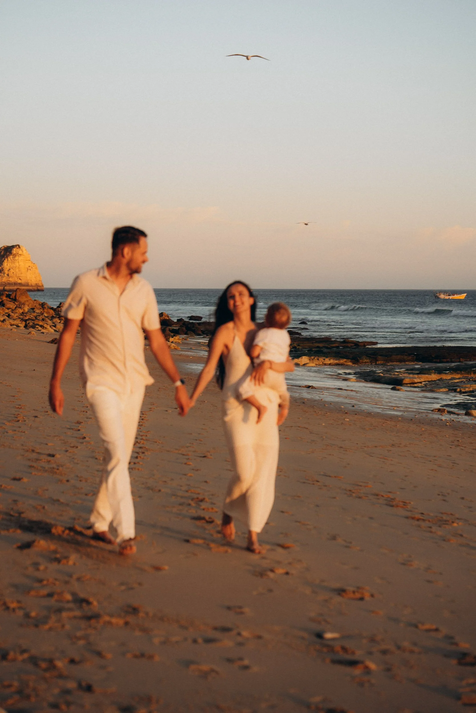 Parents walking with child by the ocean — candid family photography Algarve coast