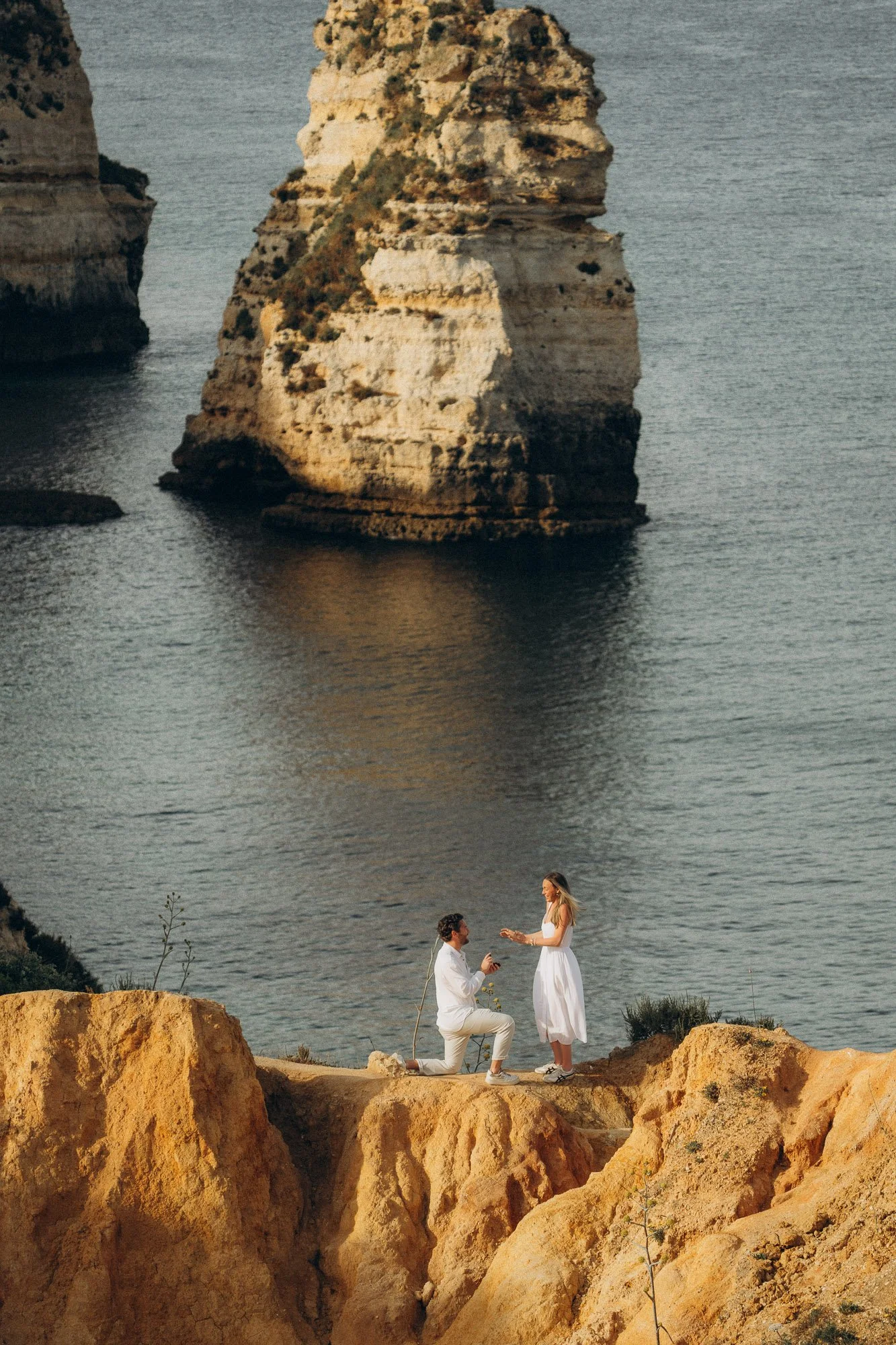 Surprise proposal photographer Algarve, man on one knee on cliff at Ponta da Piedade Lagos, iconic rock stacks