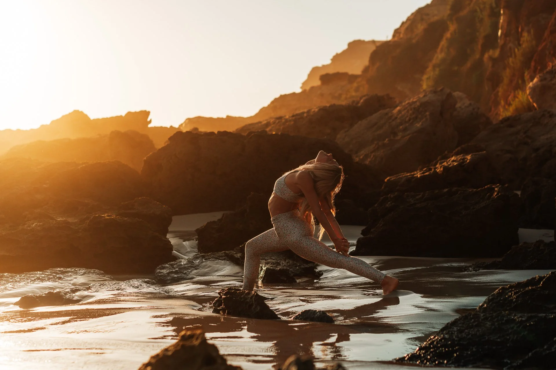 Sunset yoga flow on the shoreline, a powerful lunge reflected in wet sand with golden light over the Atlantic.
