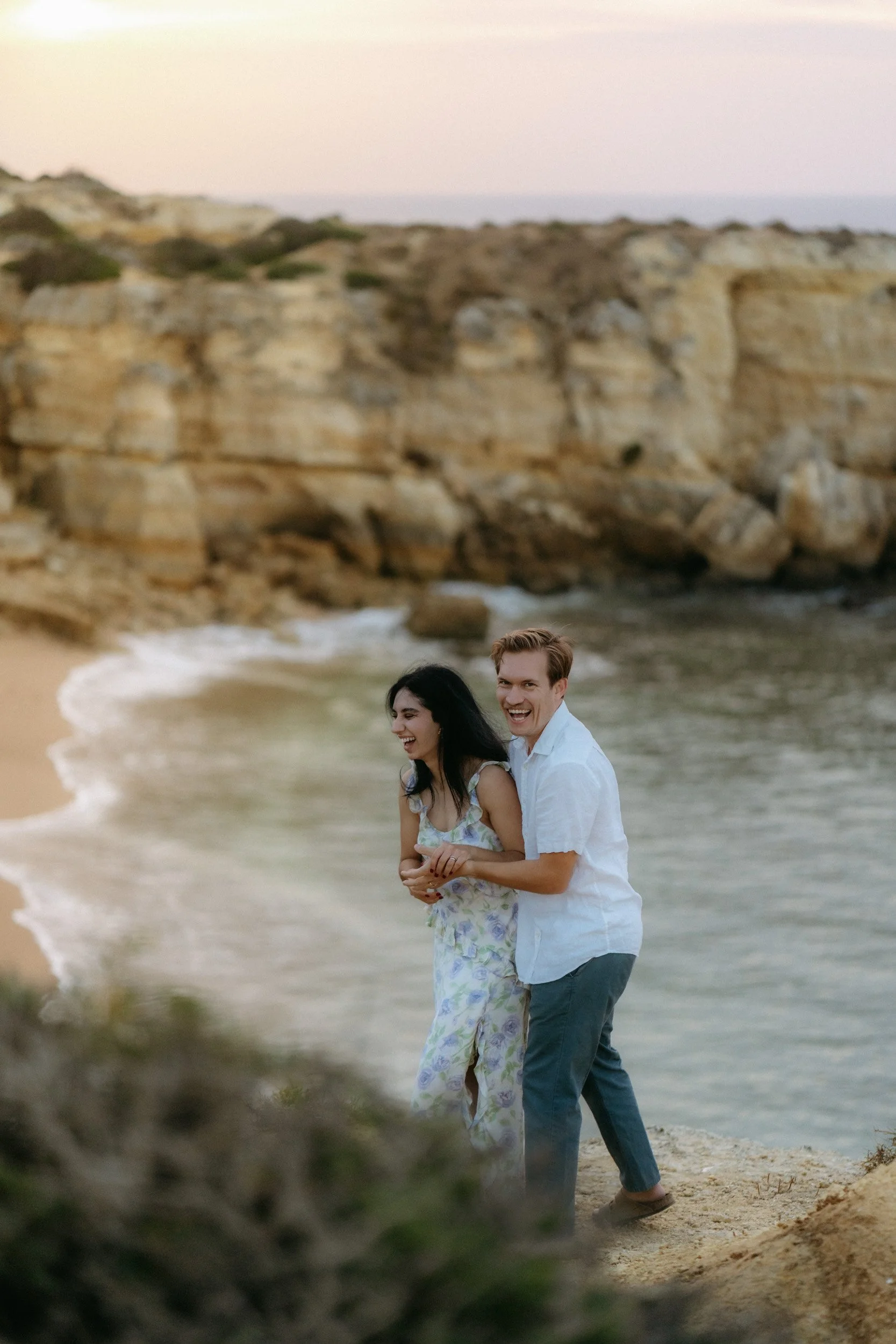 Laughing together with the ocean behind them — natural energy and spontaneous emotion above the secluded beach.