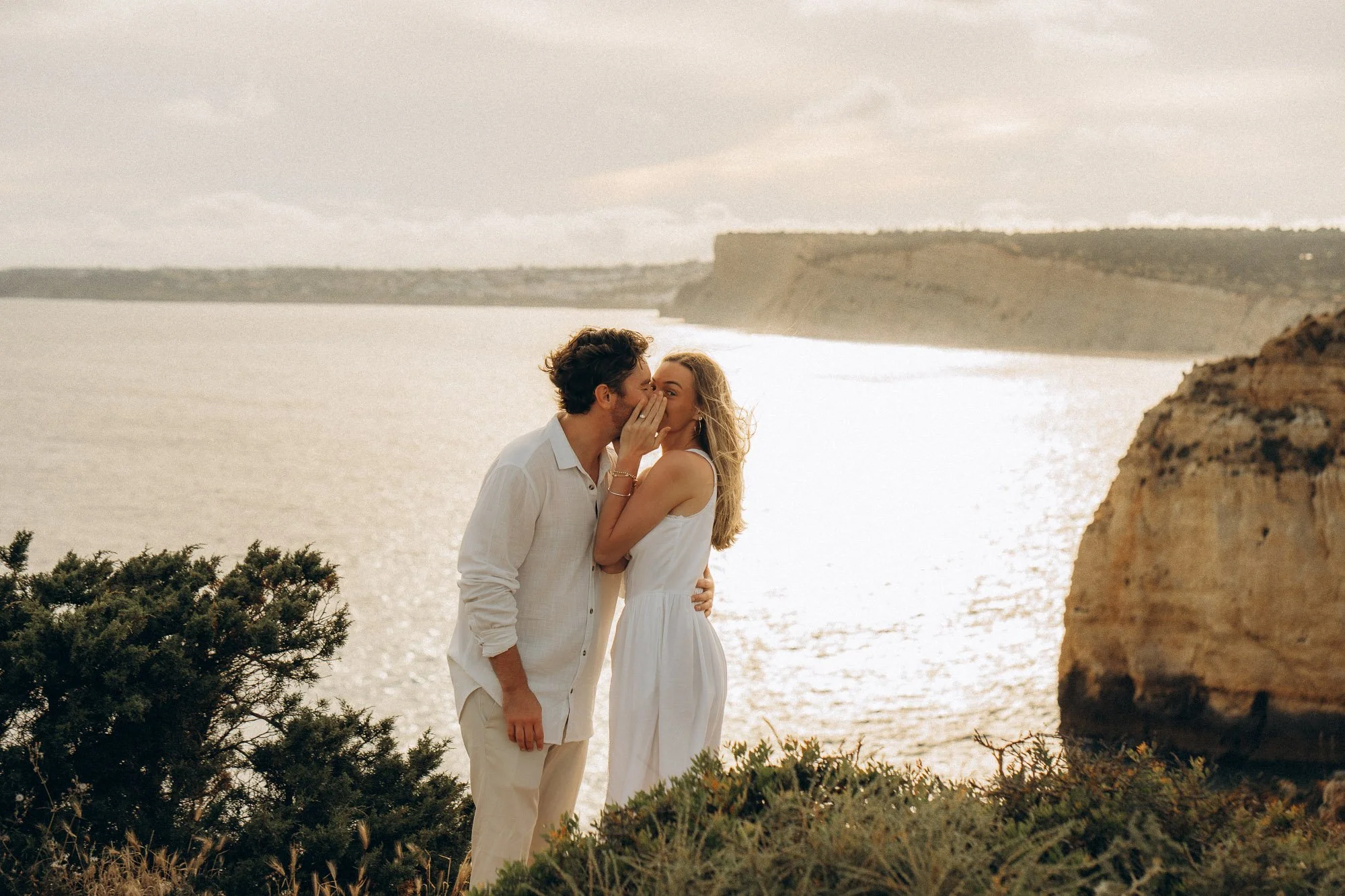 Couple kissing on Algarve clifftop overlooking ocean, engagement session natural light Portugal