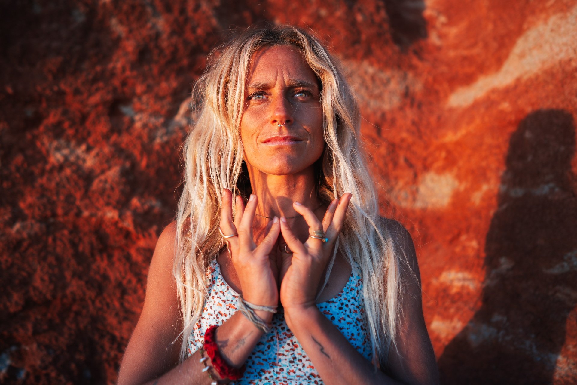 Close-up yoga portrait in warm sunset light, with a calm expression and grounded presence, against a red coastal cliff.