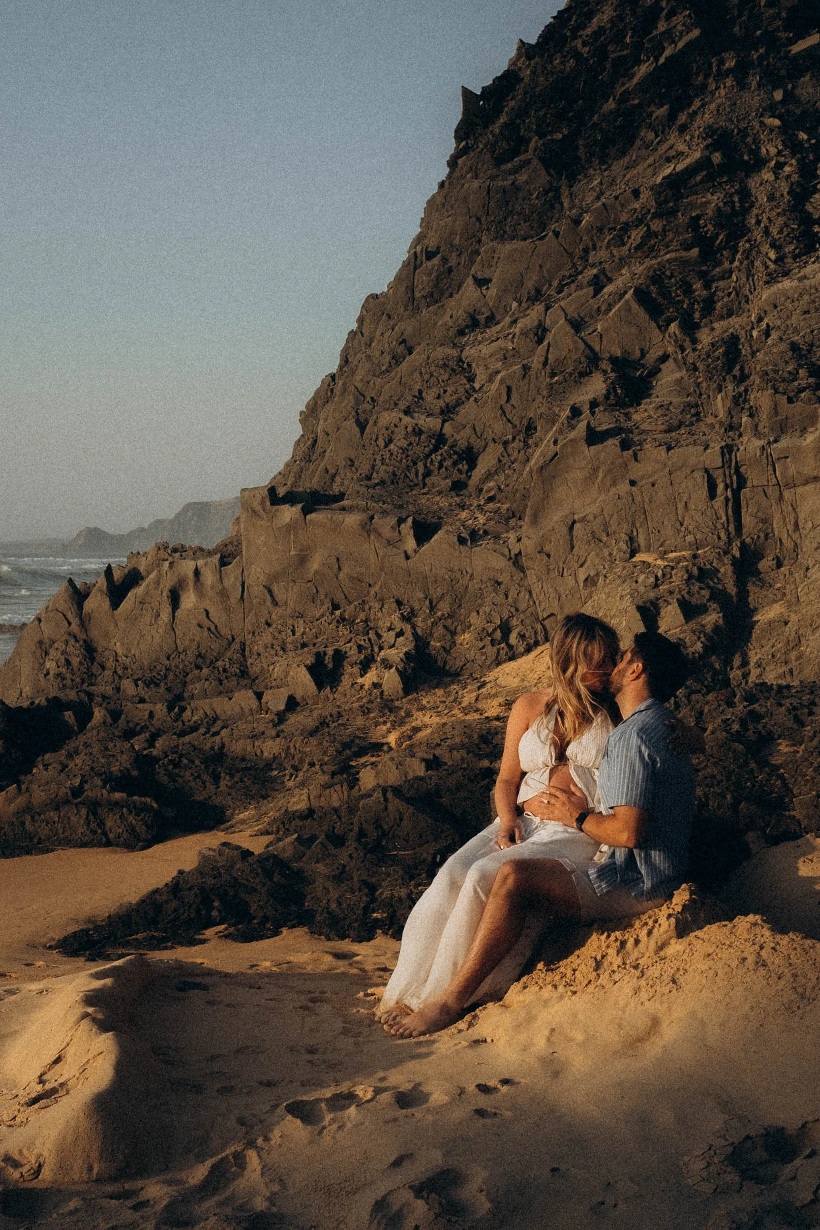 A couple kissing on the beach at sunset, sitting on a large rock