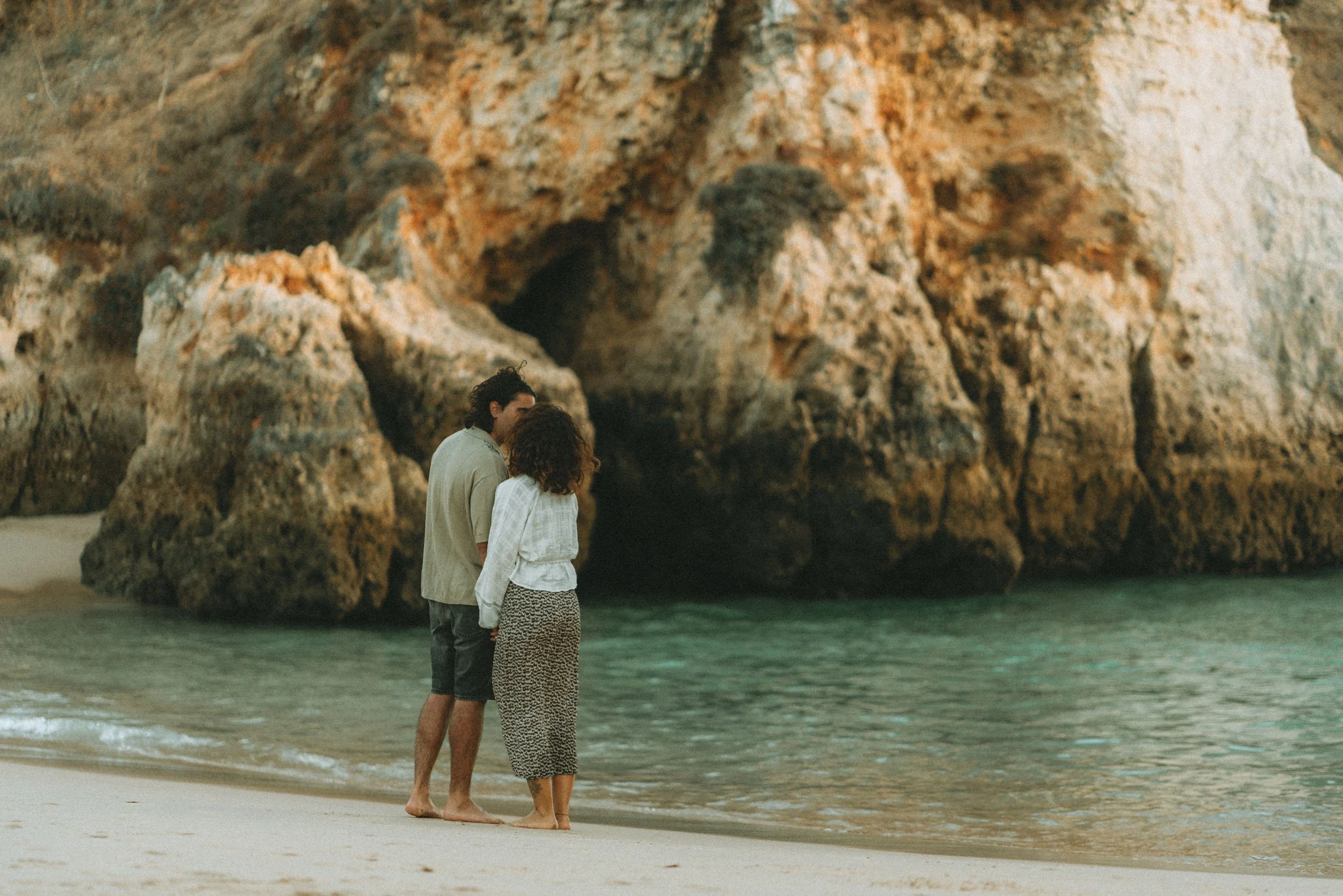 Couple dancing barefoot on the beach in Algarve, playful engagement session with cliffs and waves in the background.