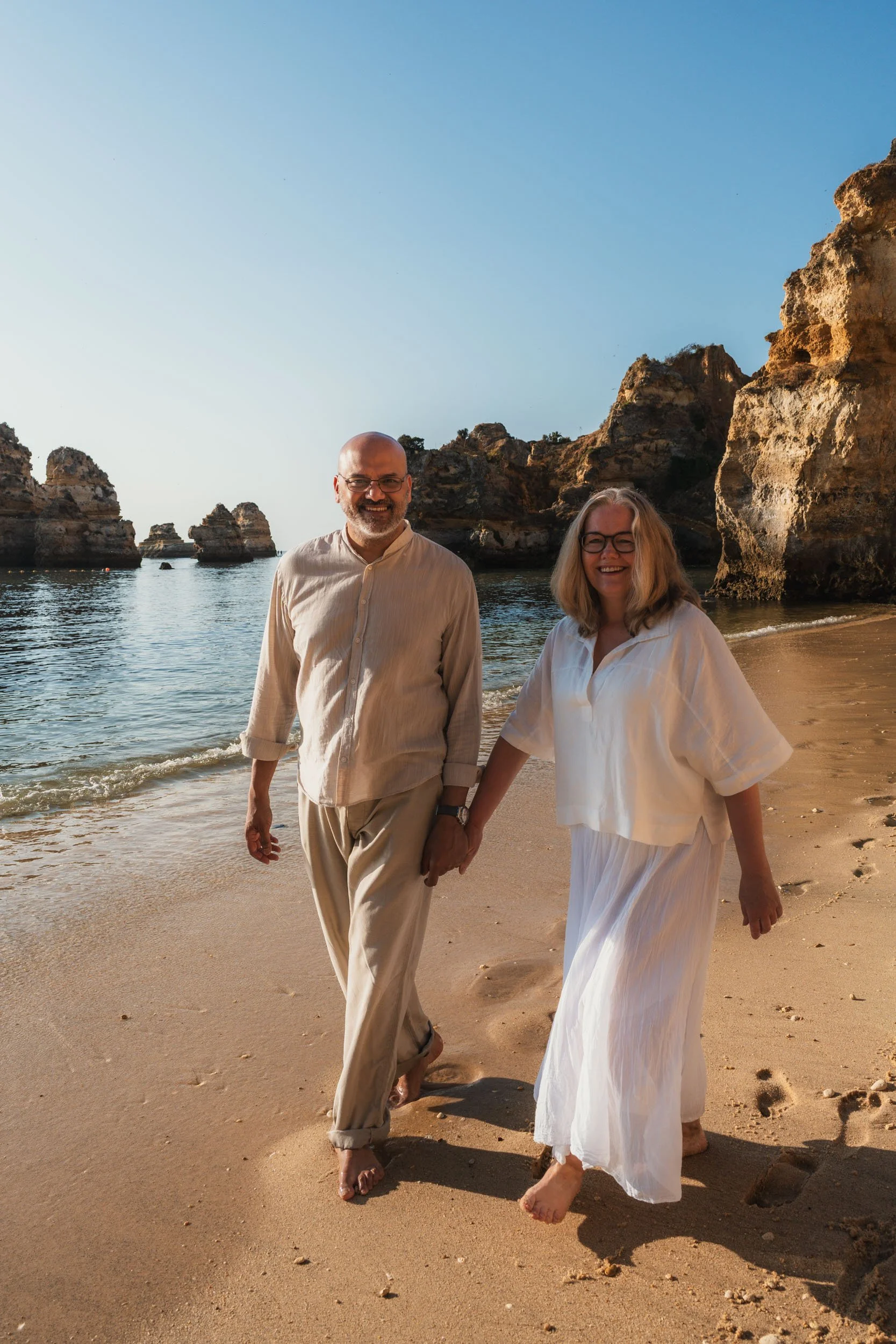 A couple walking on Praia do Camilo beach in Lagos, Algarve at sunrise.
