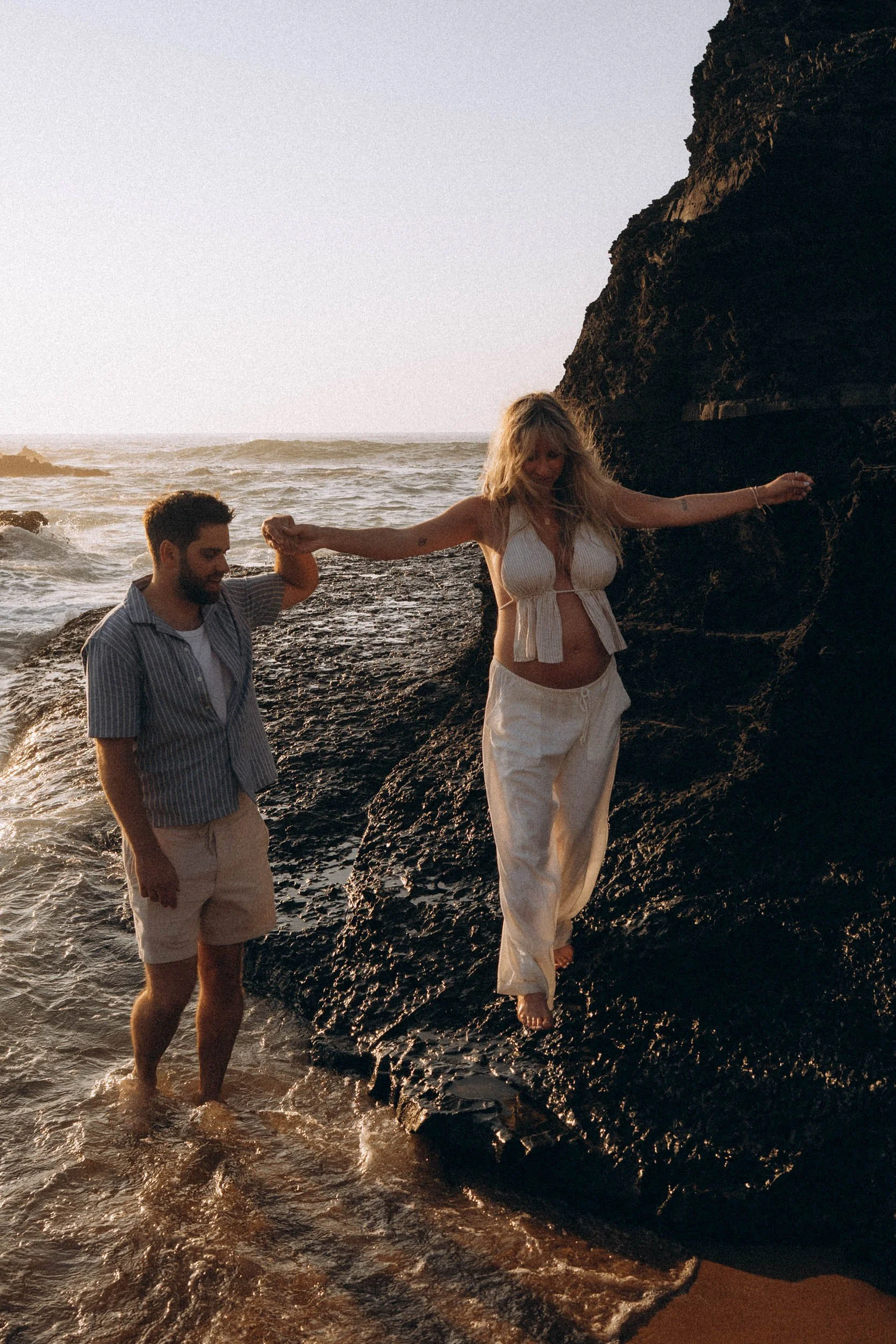 Couple lifestyle photoshoot exploring coastal rocks at Praia do Castelejo, Algarve — playful natural movement captured by local photographer.