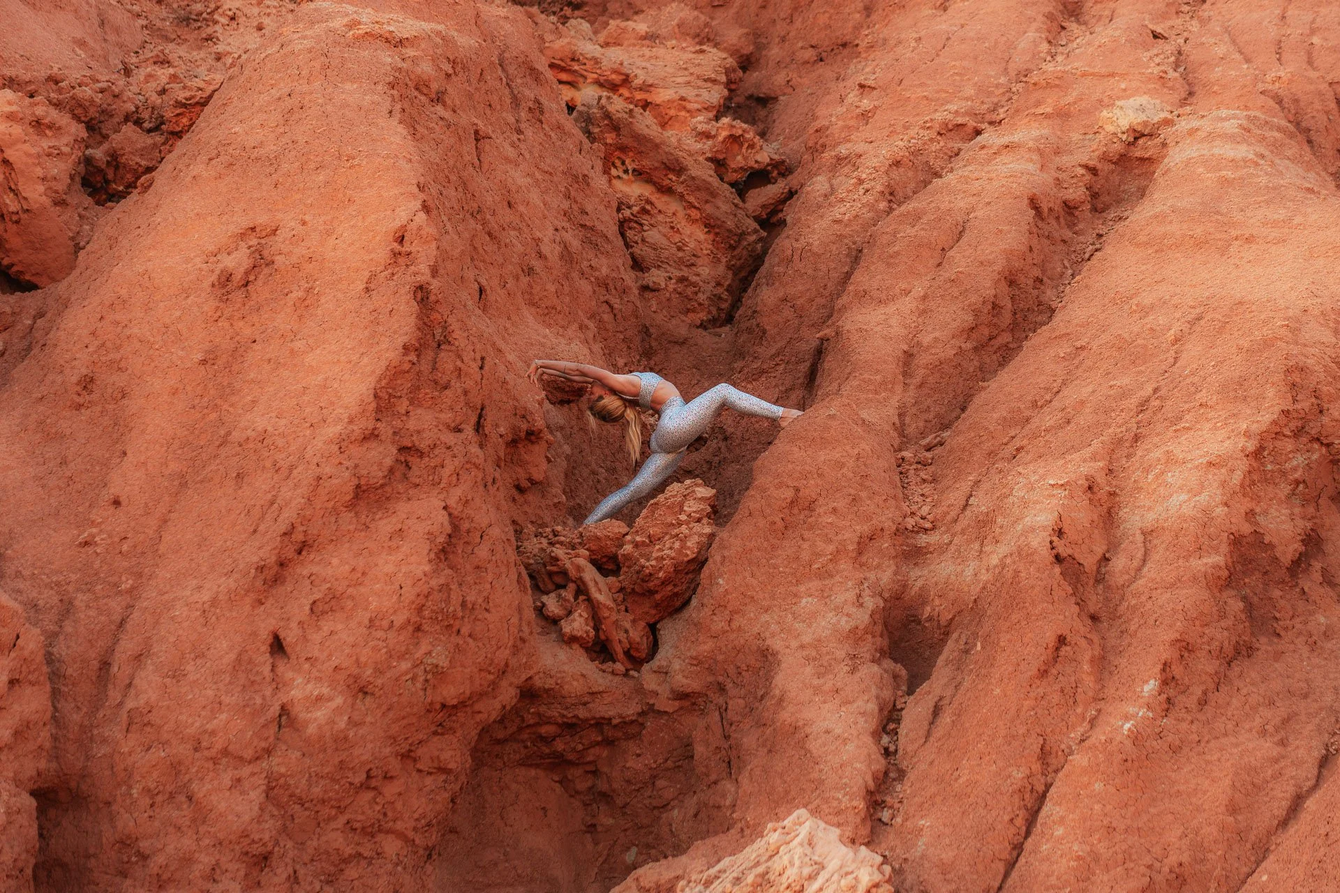 Dynamic yoga stretch between red sandstone walls, strength and flexibility expressed in a natural Algarve landscape.