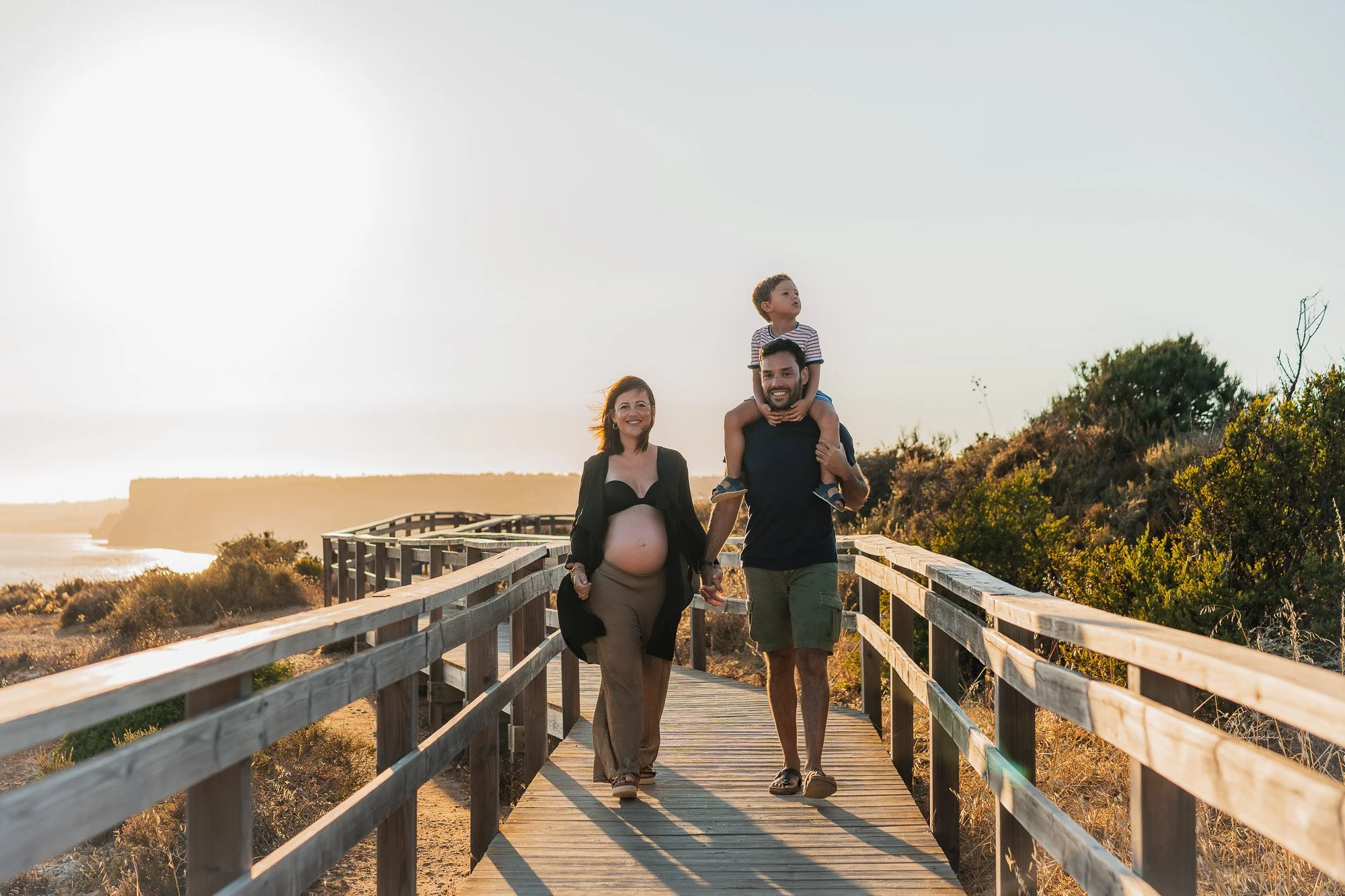 Family of 3 with baby bump smiling on the dramatic cliffs of Ponta da Piedade, Lagos, Algarve.