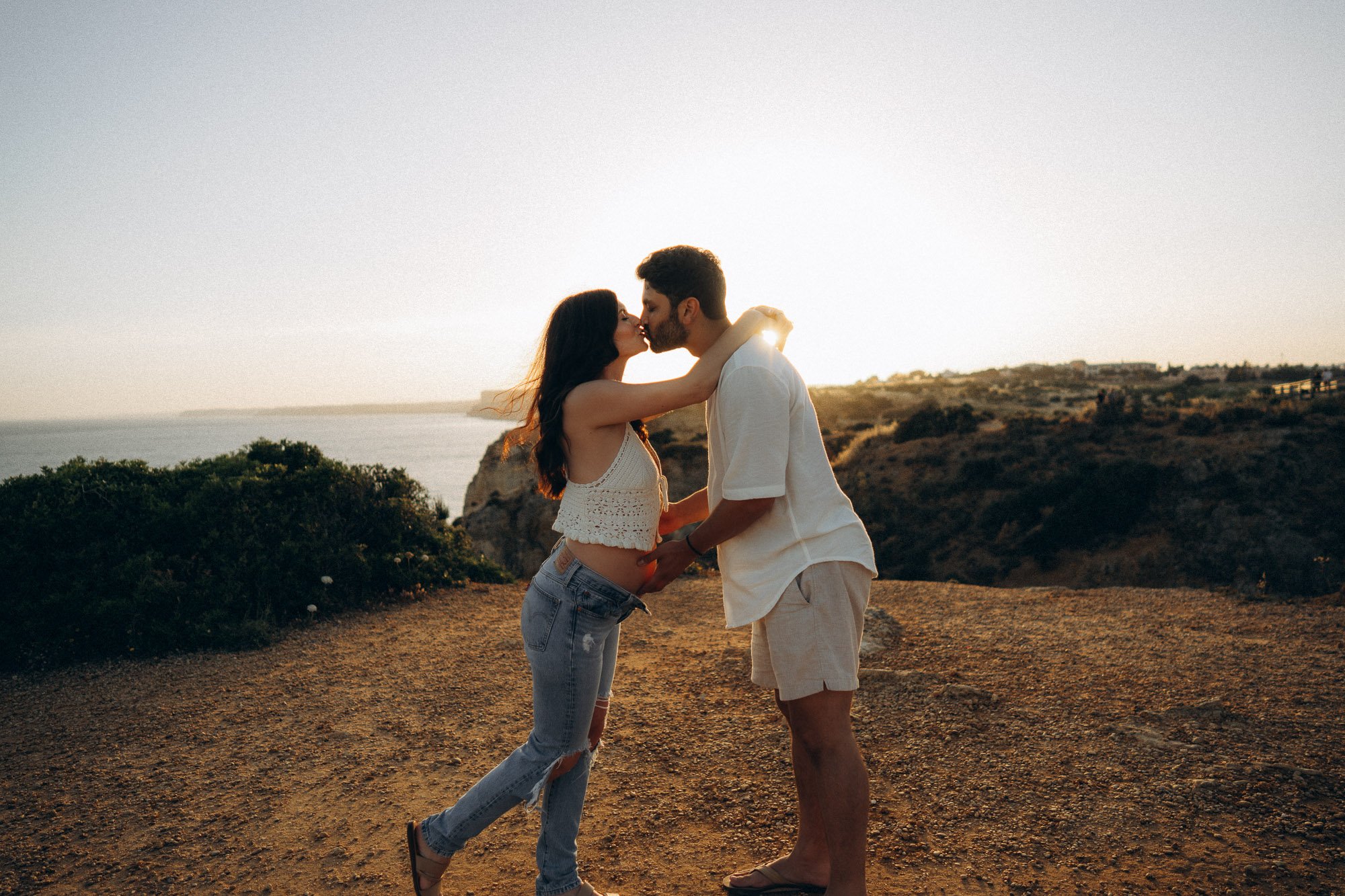 Couple kissing on Algarve clifftop at sunset, ocean and coastline view, couples session Portugal