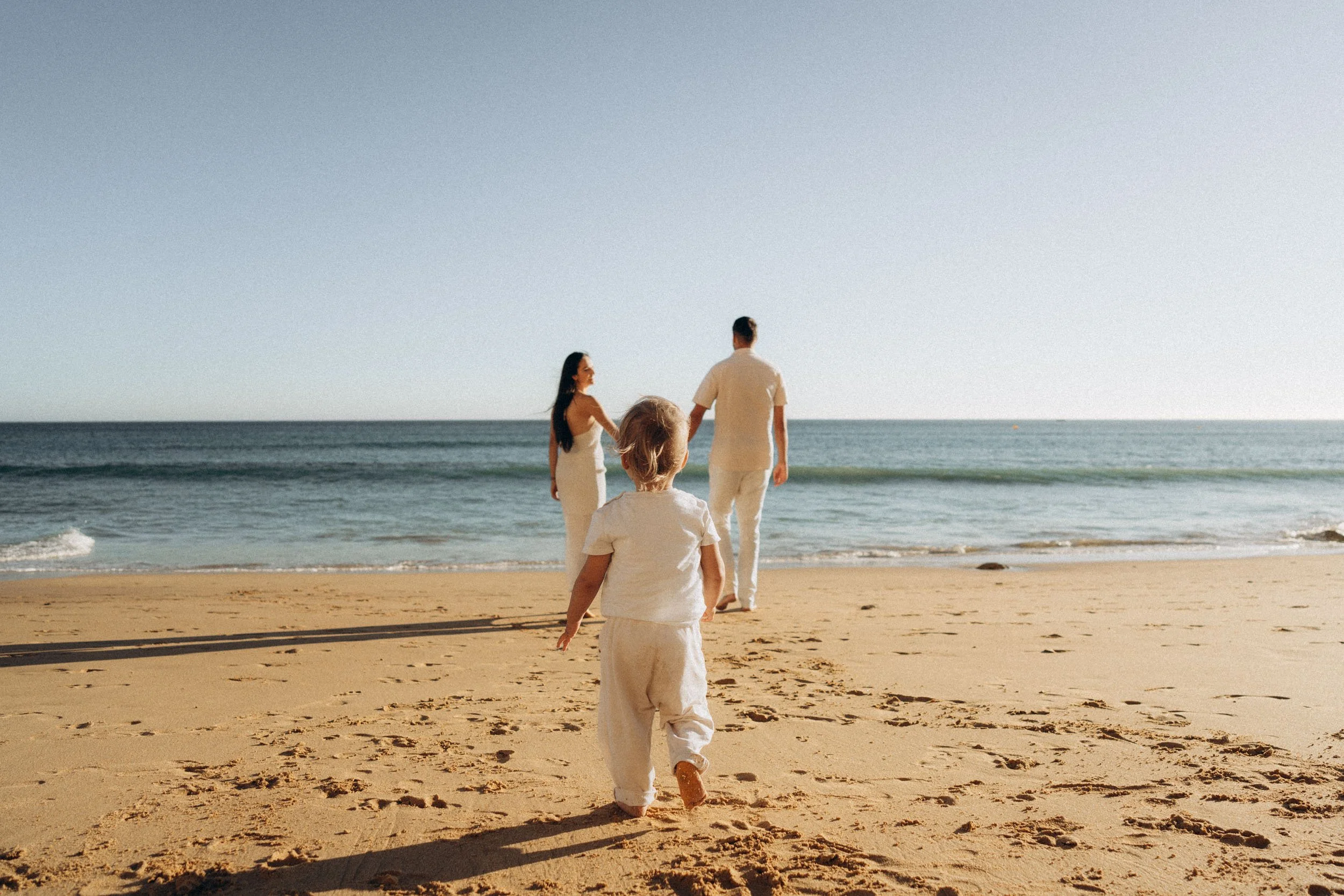 Child walking toward parents during a beach family photoshoot in Lagos, Algarve
