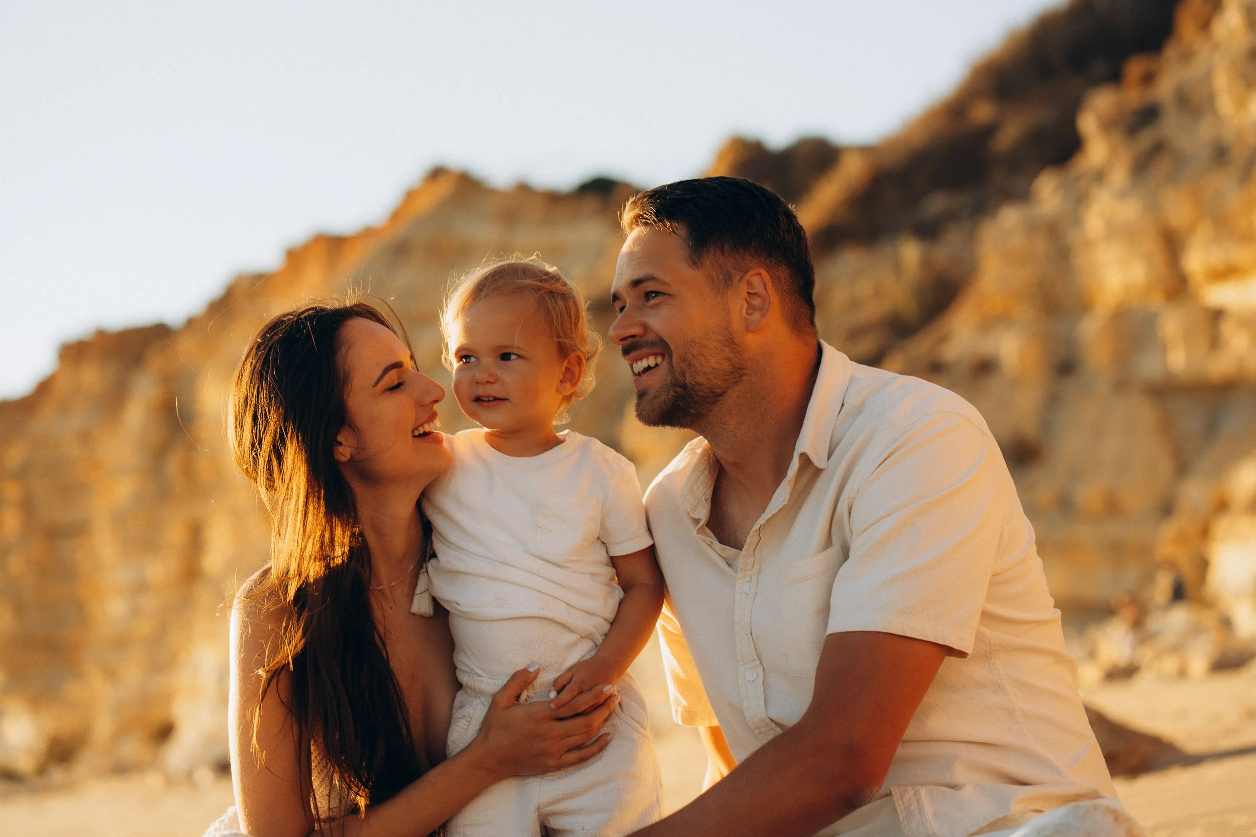 Natural portrait of a family of 3 hugging in Porto de Mòs, Lagos. Golden hour in the Algarve.