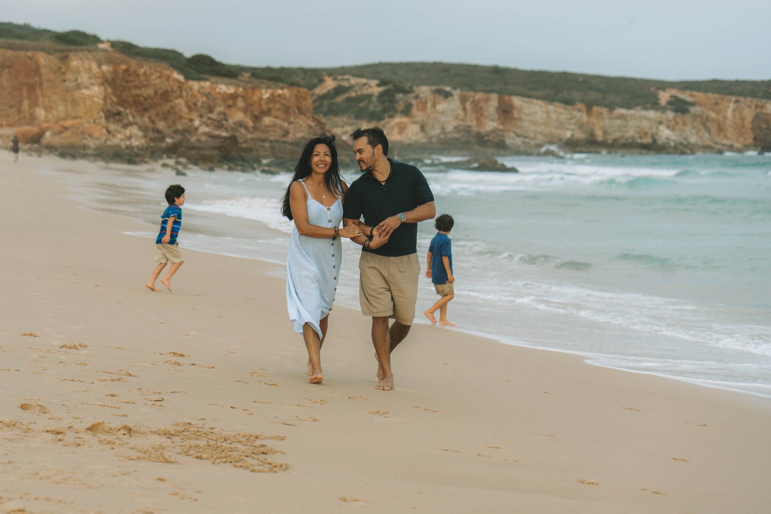 A couple walking together while the kids play freely in the background, showing the relaxed rhythm of a family photoshoot at Martinhal.