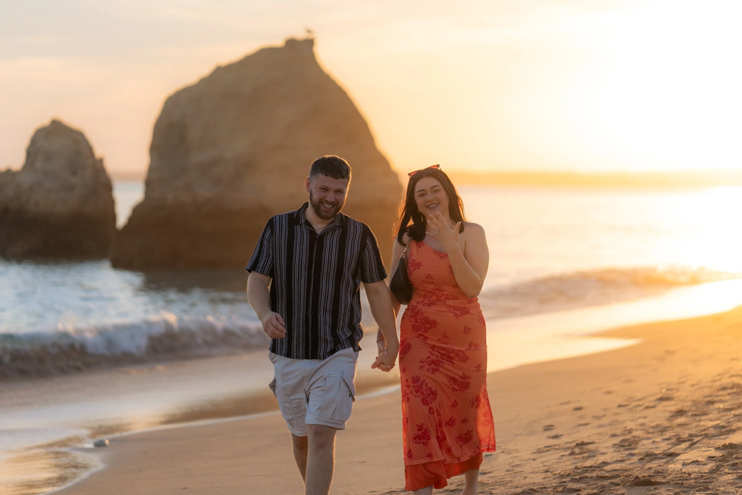 Walking along the shoreline after the proposal — natural movement, warm reflections on the sand and the iconic Algarve cliffs behind them.