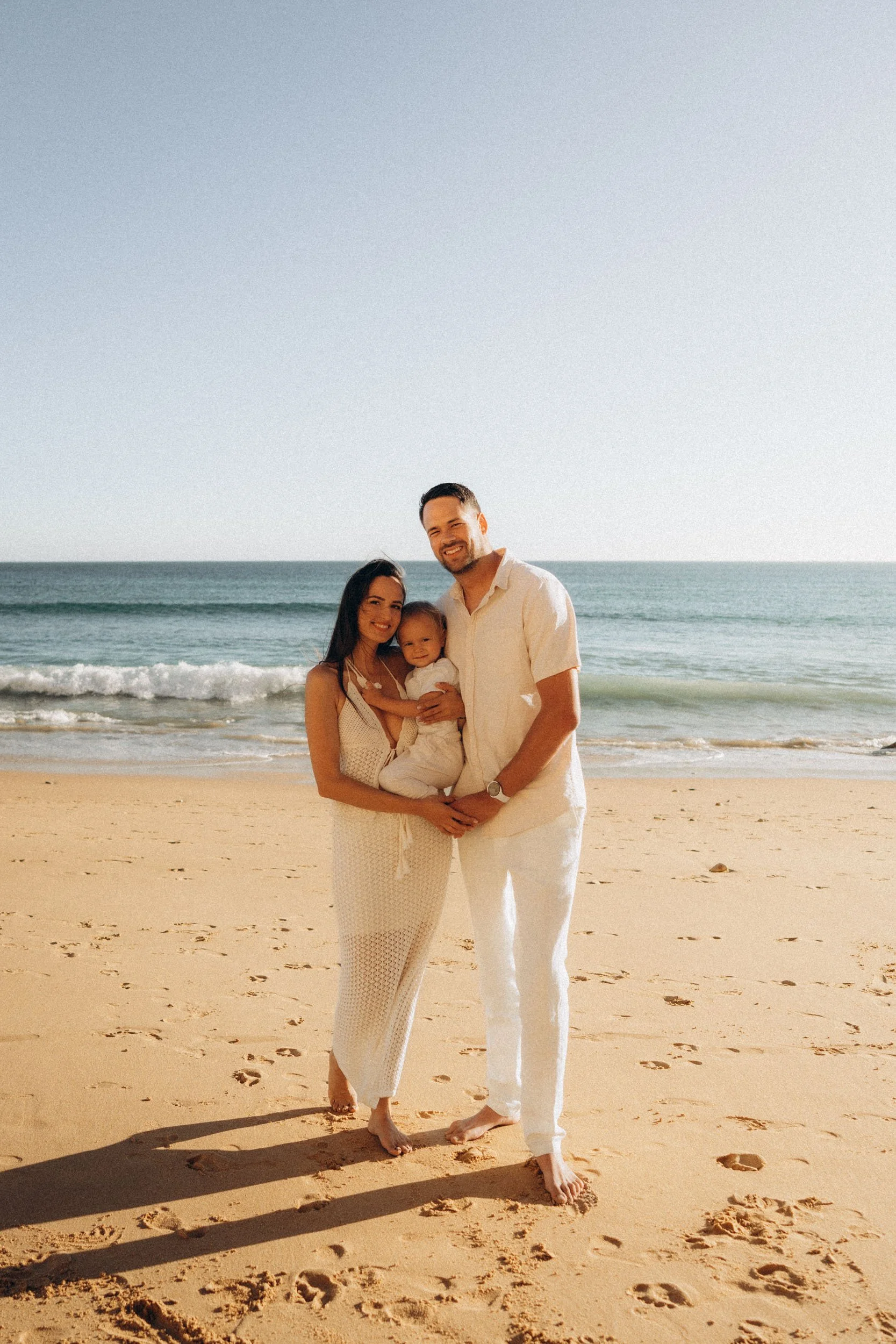 Family photoshoot at Porto de Mos beach in Lagos, Algarve by family photographer — parents holding child on sandy beach
