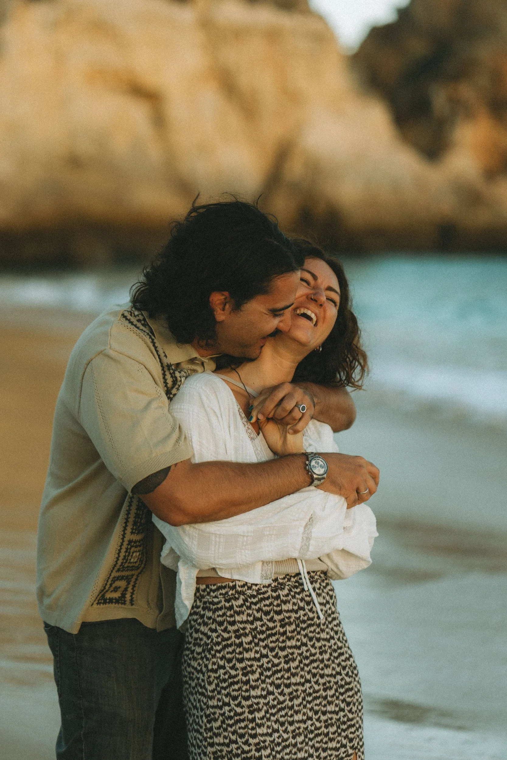 Playful and intimate moment between a couple by the shoreline at Praia dos Três Irmãos, natural expressions and soft evening tones.