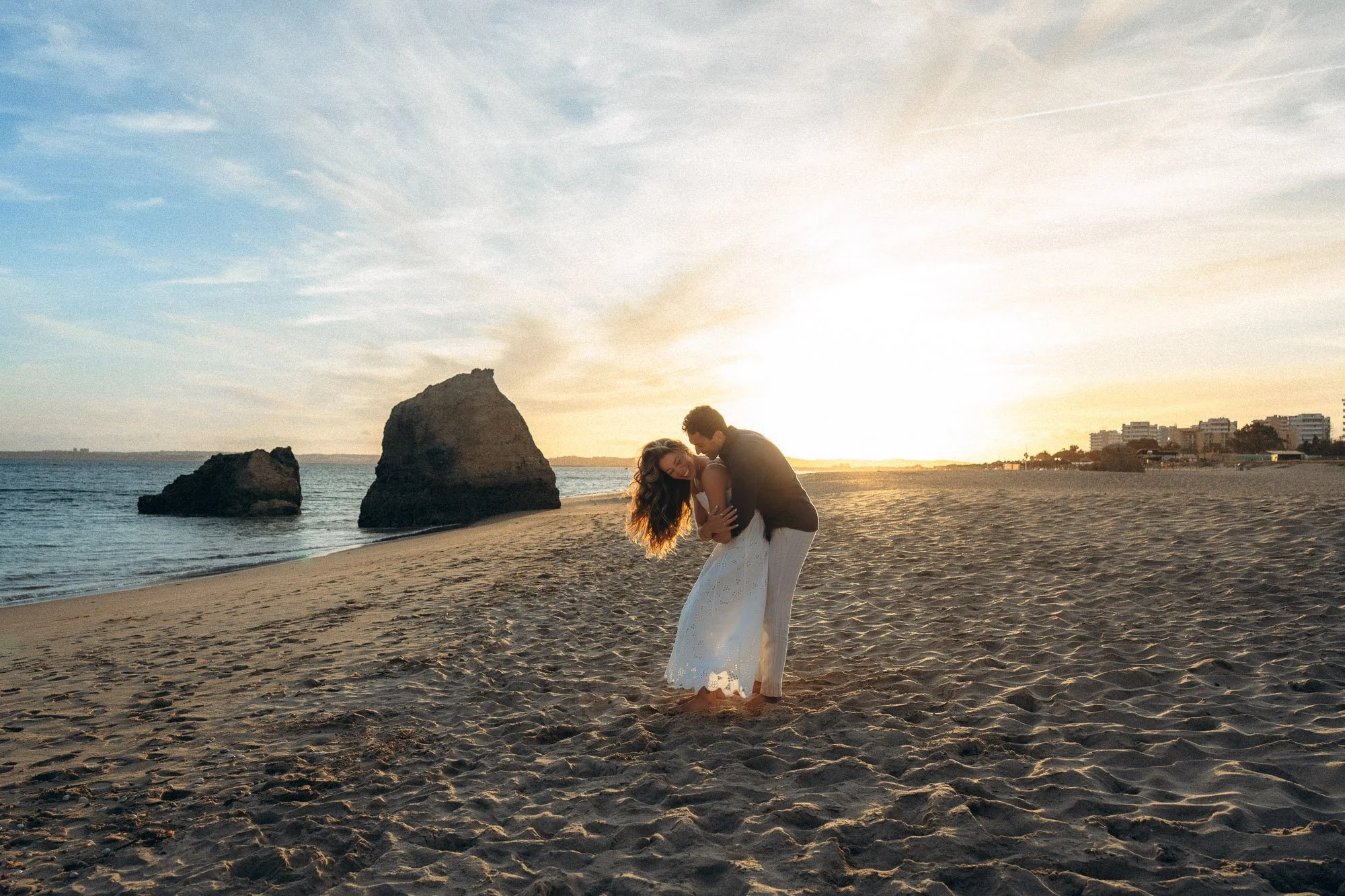 Couple dip kiss on Algarve beach at sunset with sea stack in background, engagement photographer Portugal