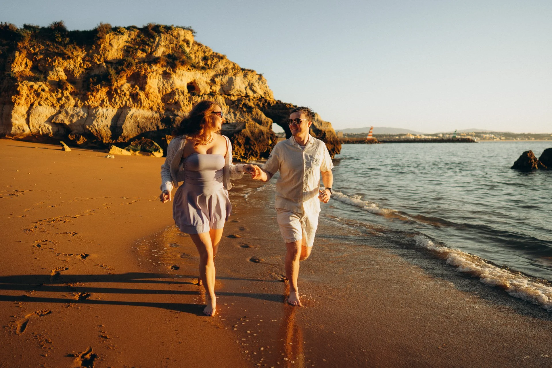 Couple walking on the beach at Praia dos Estudiantes during golden hour photoshoot in the Algarve
