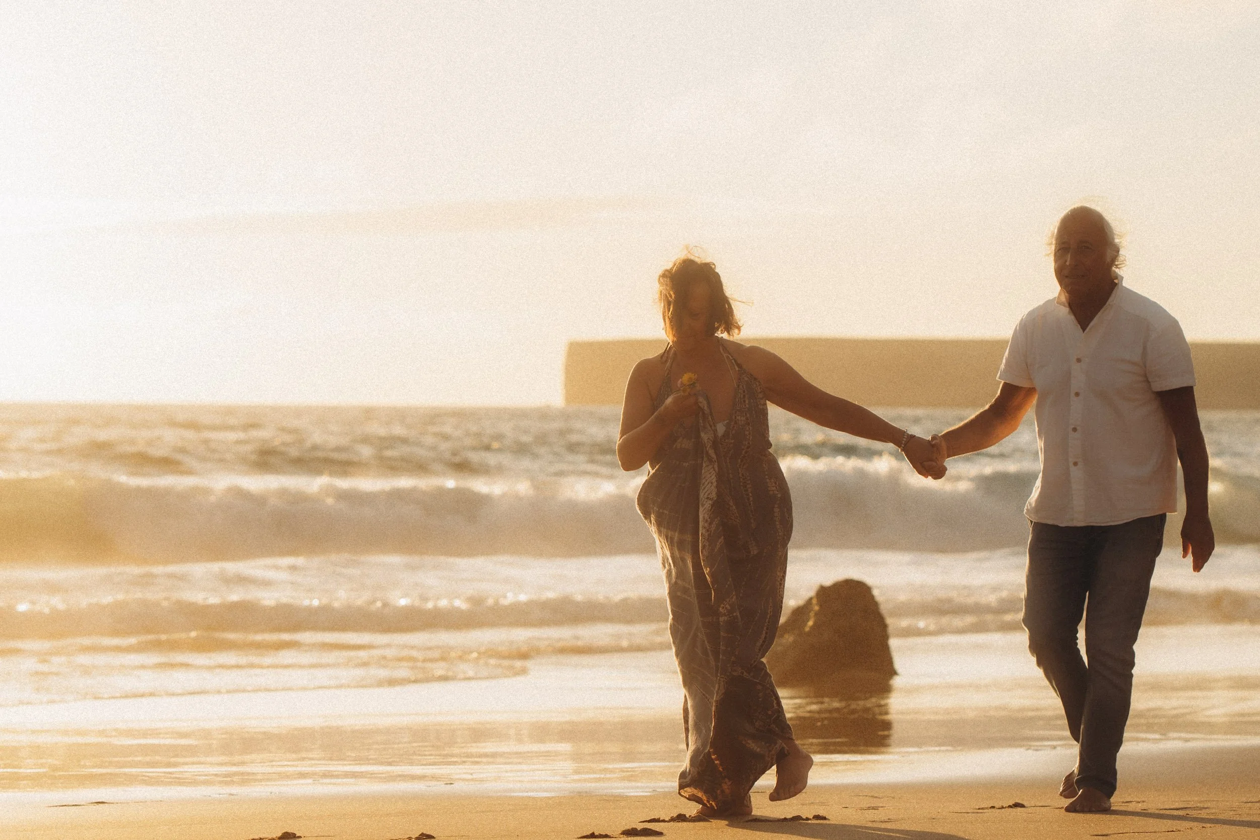 Couple holding hands while walking along Praia do Tonel beach at sunset in Sagres.