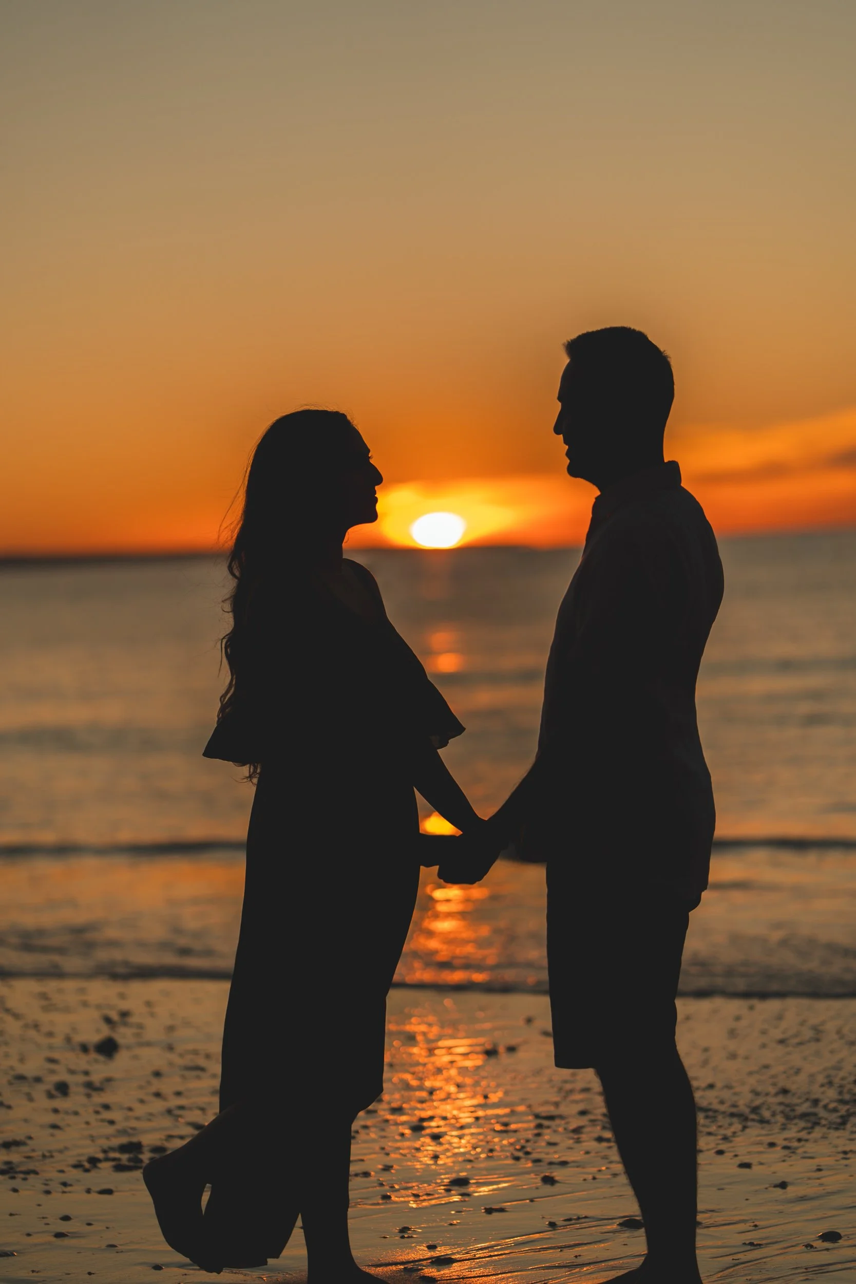 Romantic silhouette at sunset on Praia Dona Ana, couple holding hands with the Algarve sun setting over the Atlantic Ocean.