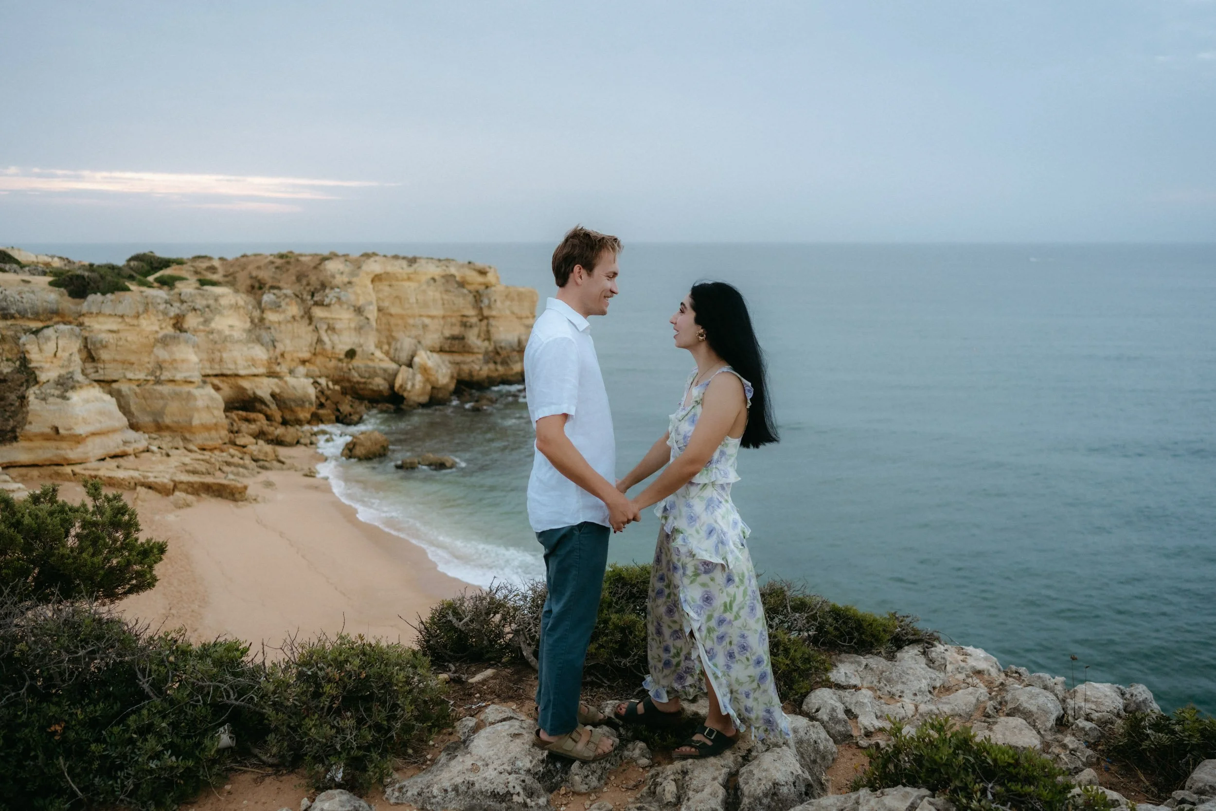 Holding hands on the edge of the cliffs with panoramic sea views. A calm, cinematic moment above Praia da Coelha.