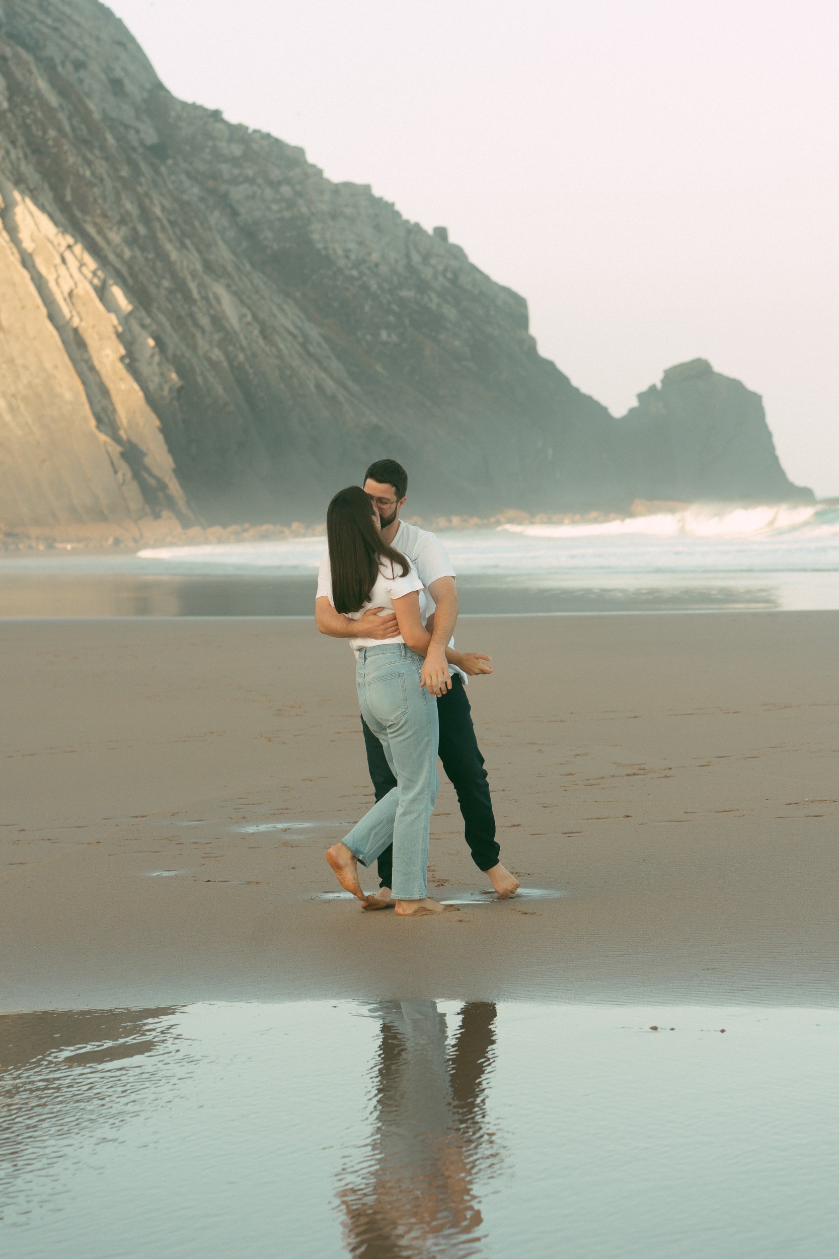 Romantic couple embracing on Praia do Castelejo beach in Algarve, Portugal during golden hour. Natural lifestyle couple photoshoot with cliffs and ocean in the background by Algarve photographer Giancarlo Fortuna.