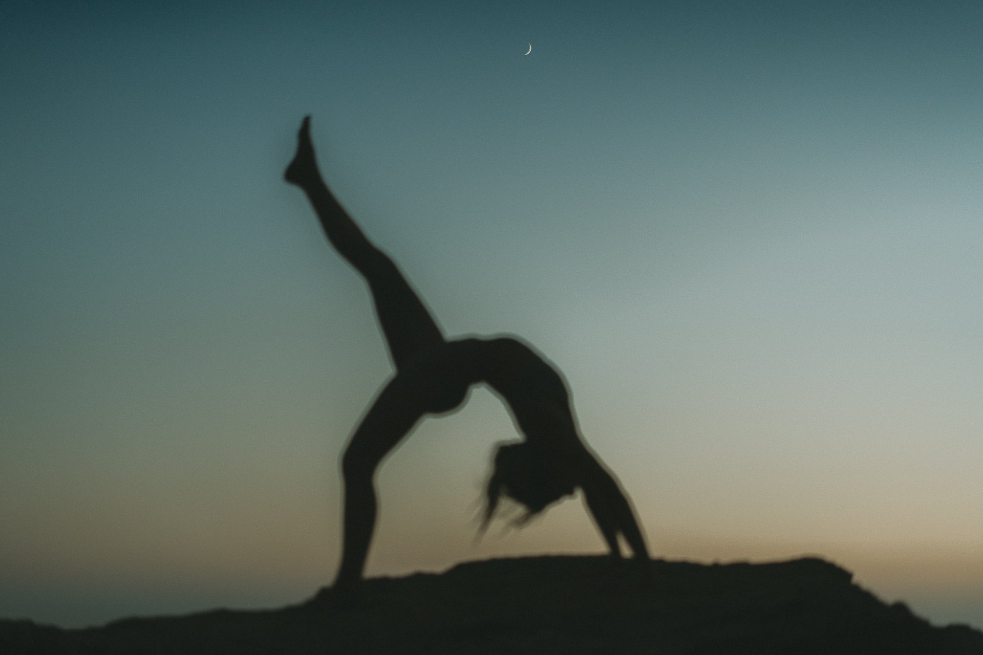 Soft-focus yoga backbend at blue hour, a meditative moment blending movement, sky, and coastal horizon.
