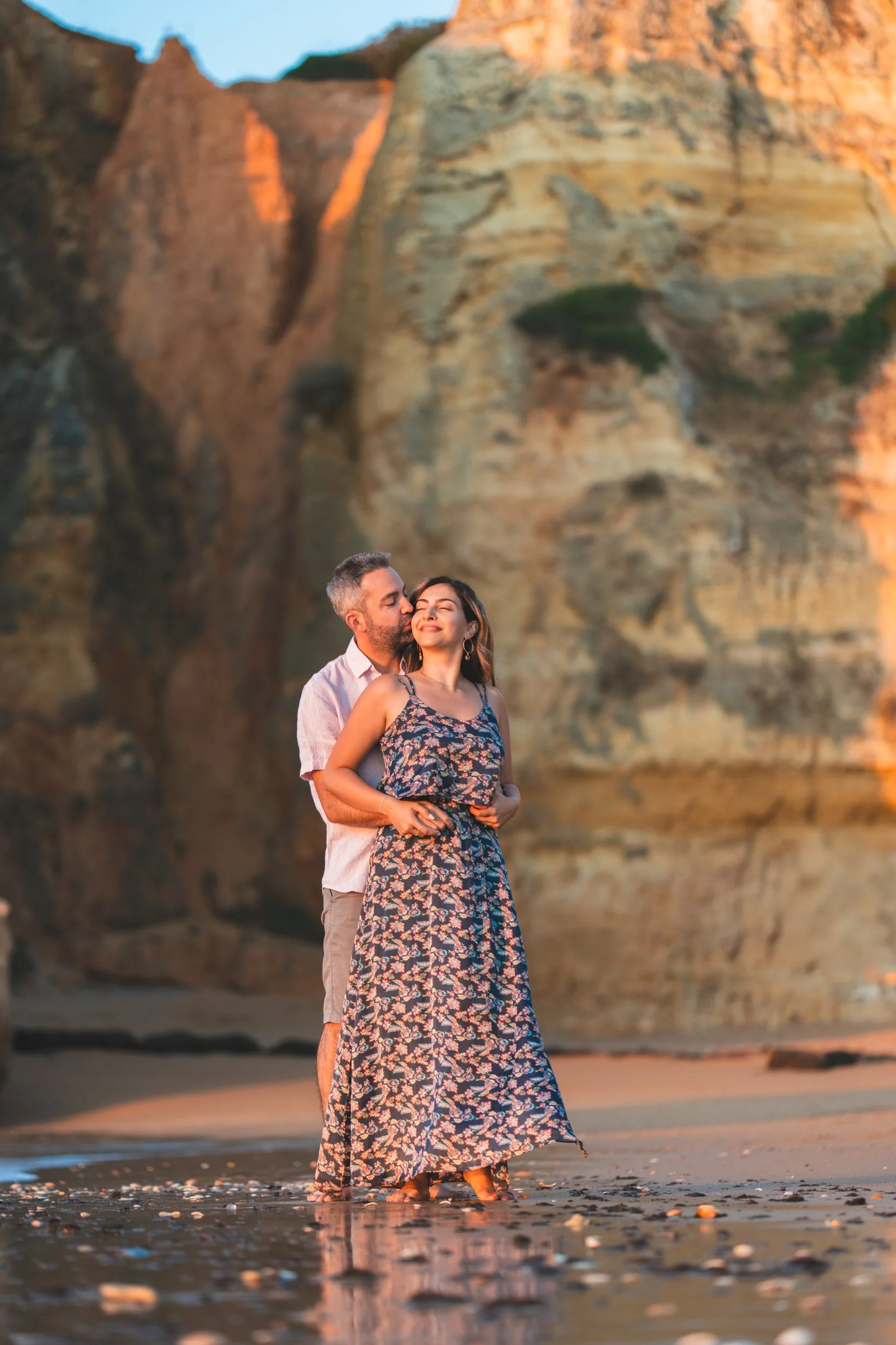 Tender kiss at golden hour on Praia Dona Ana beach, iconic rock stack glowing in warm Algarve light.