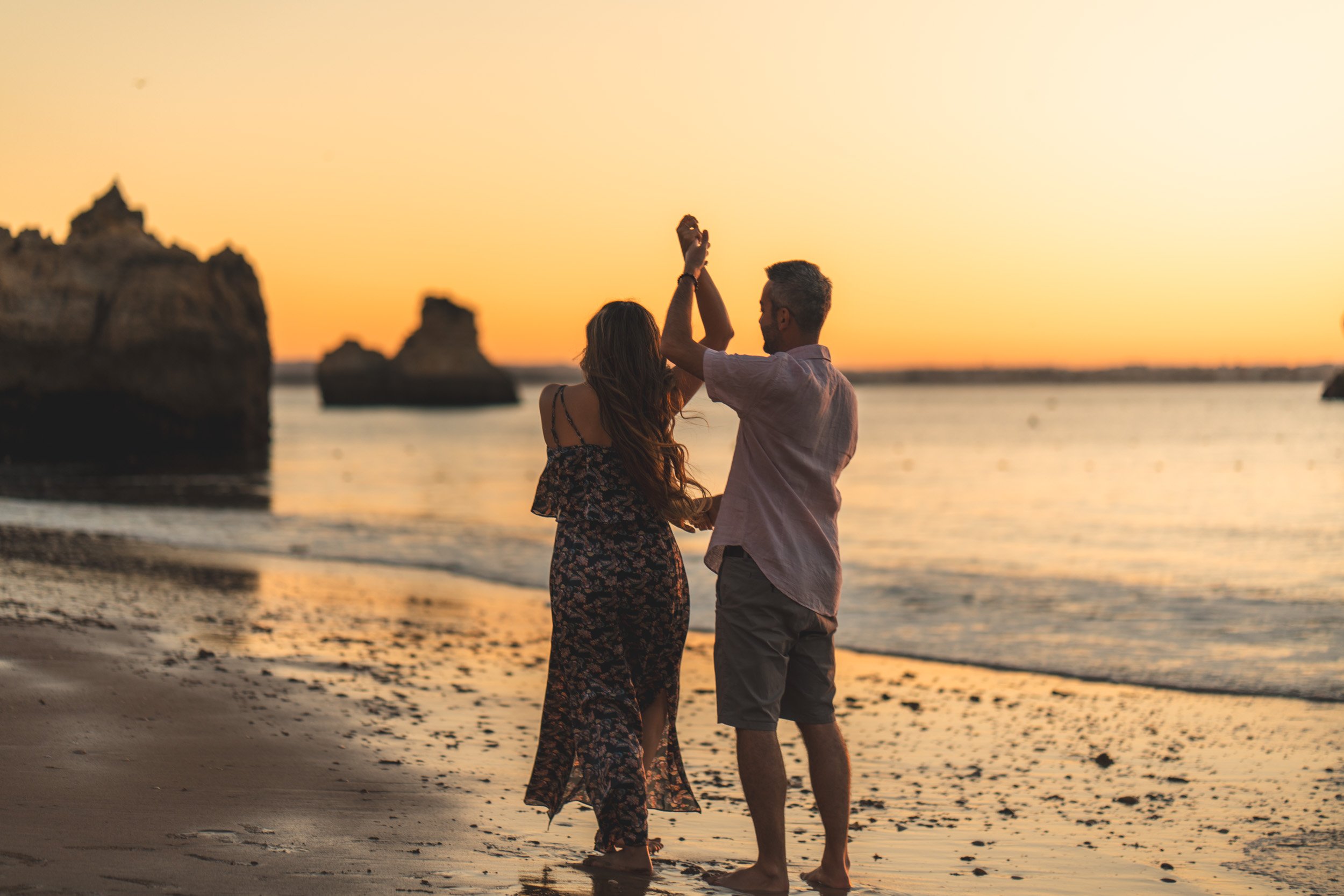 A couple dancing at sunset on Praia Dona Ana, soft waves and golden reflections creating a cinematic atmosphere.