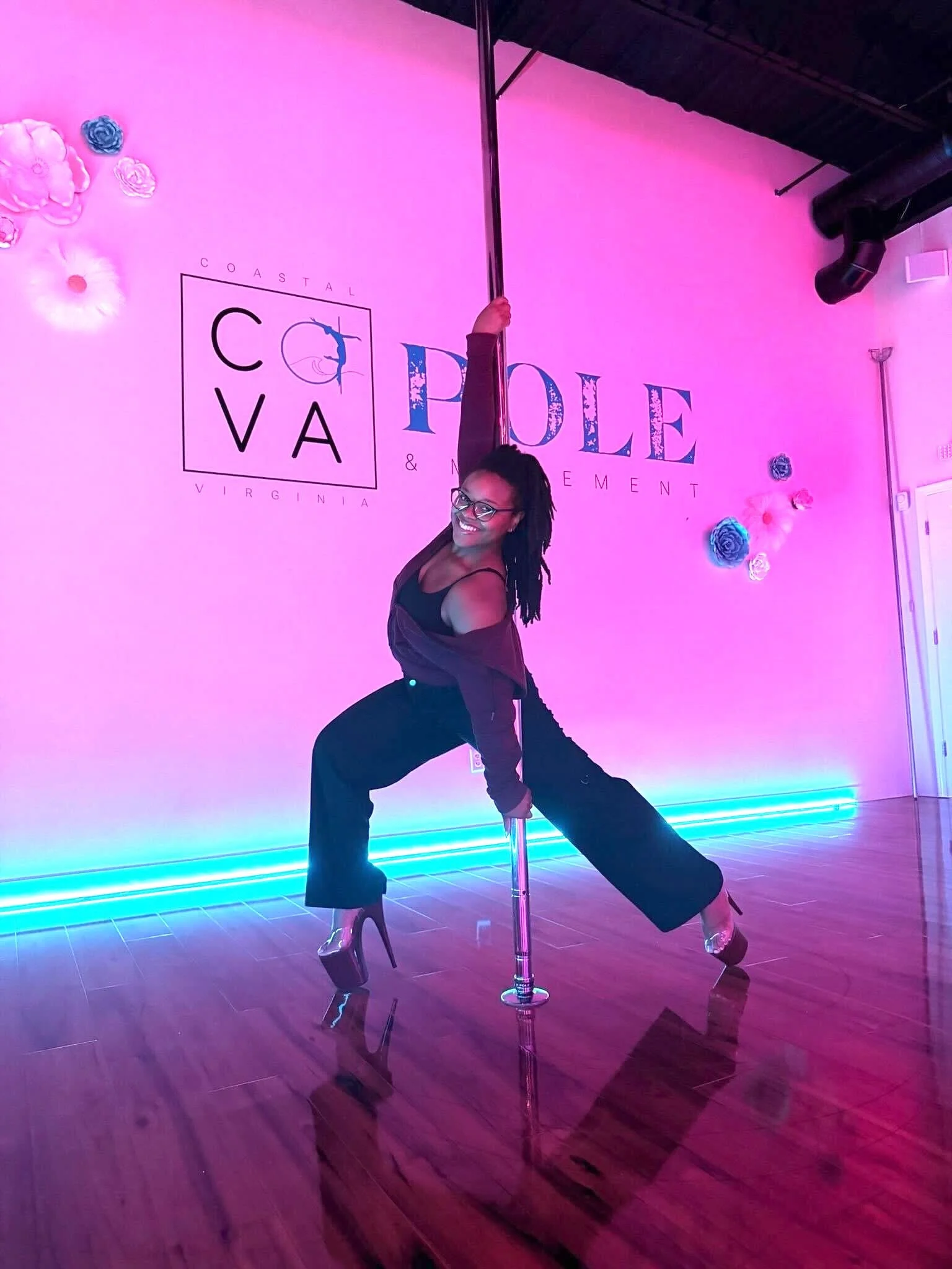 woman with braids wearing sweatsuit and dance heels does a lunge holding the pole
