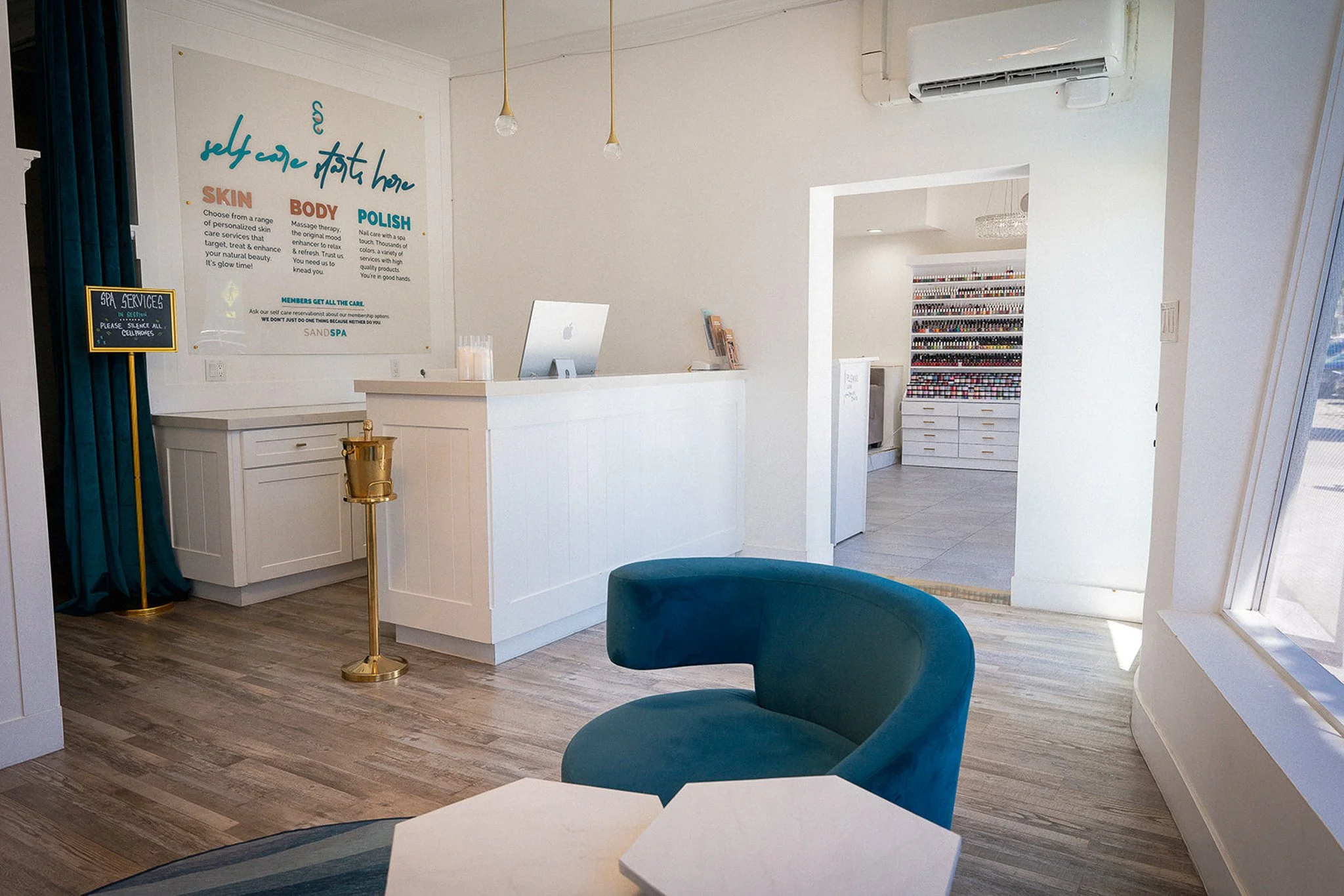 Exterior of a building with a large beach-themed window decal for a nail salon and spa. A small chalkboard sign outside offers services like massage, facials, and nails.