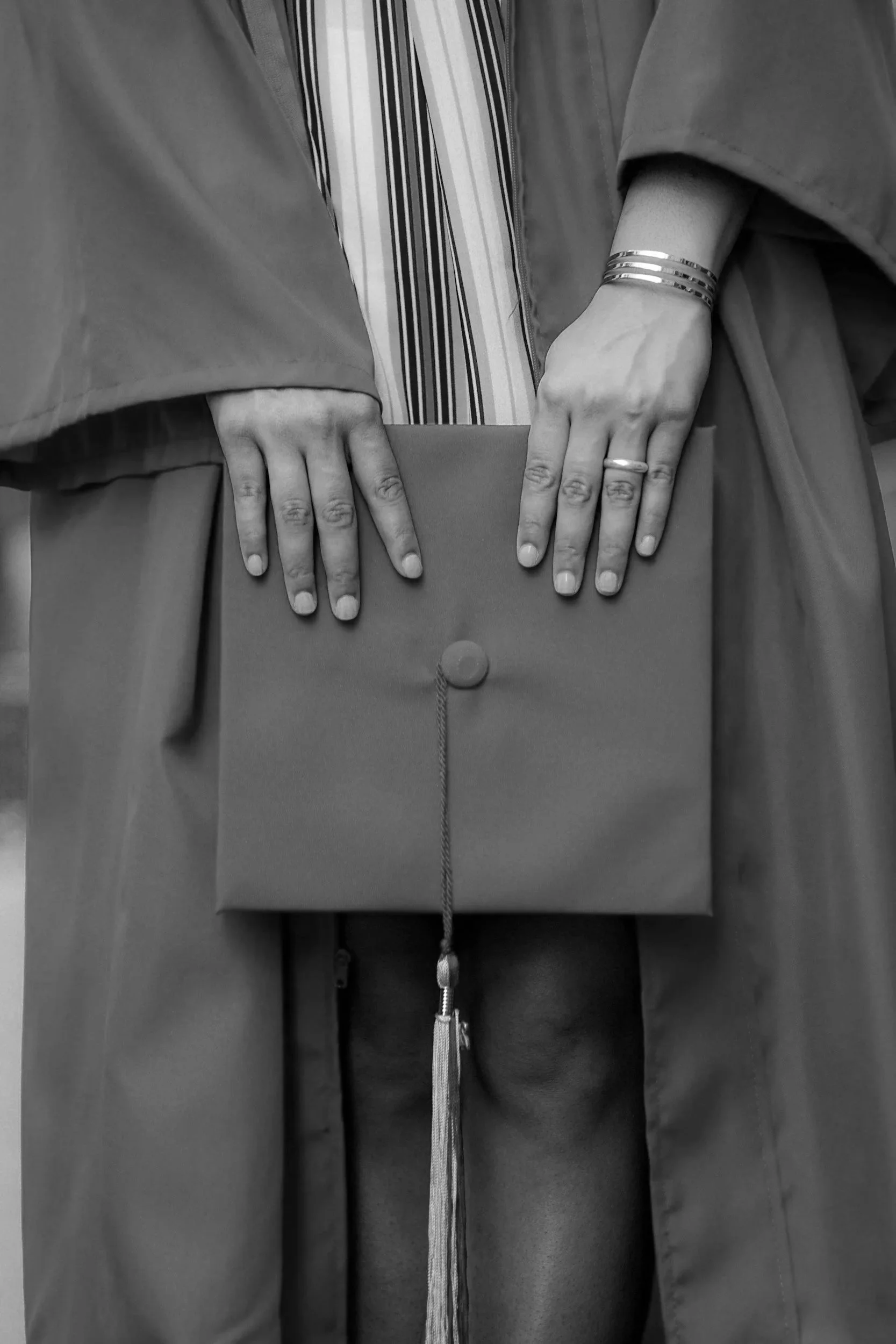 Close-up of a person holding a diploma or certificate with both hands, wearing rings and bracelets, dressed in judicial robes.