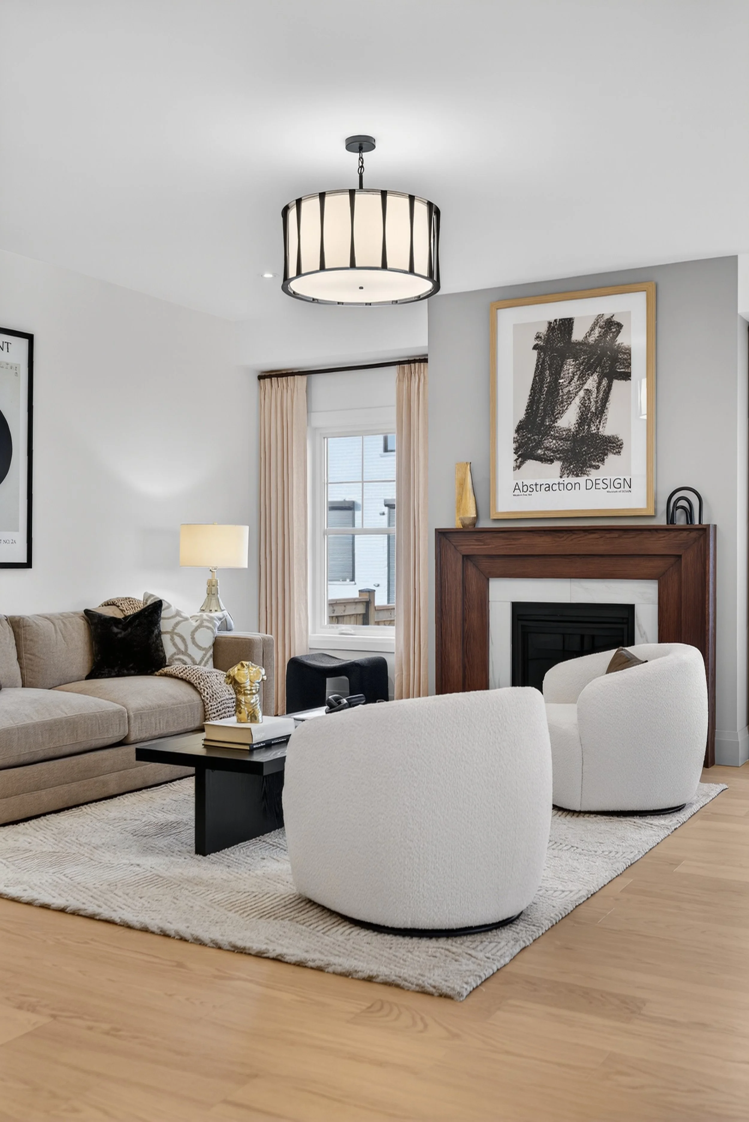 Modern living room with beige sofa, white armchairs, black coffee table, fireplace with wooden mantel, abstract artwork, beige curtains, window, and contemporary chandelier.