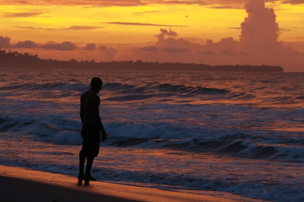 Man silhouetted by sunset looks out over ocean. Photo by Kubiari Alfredo.