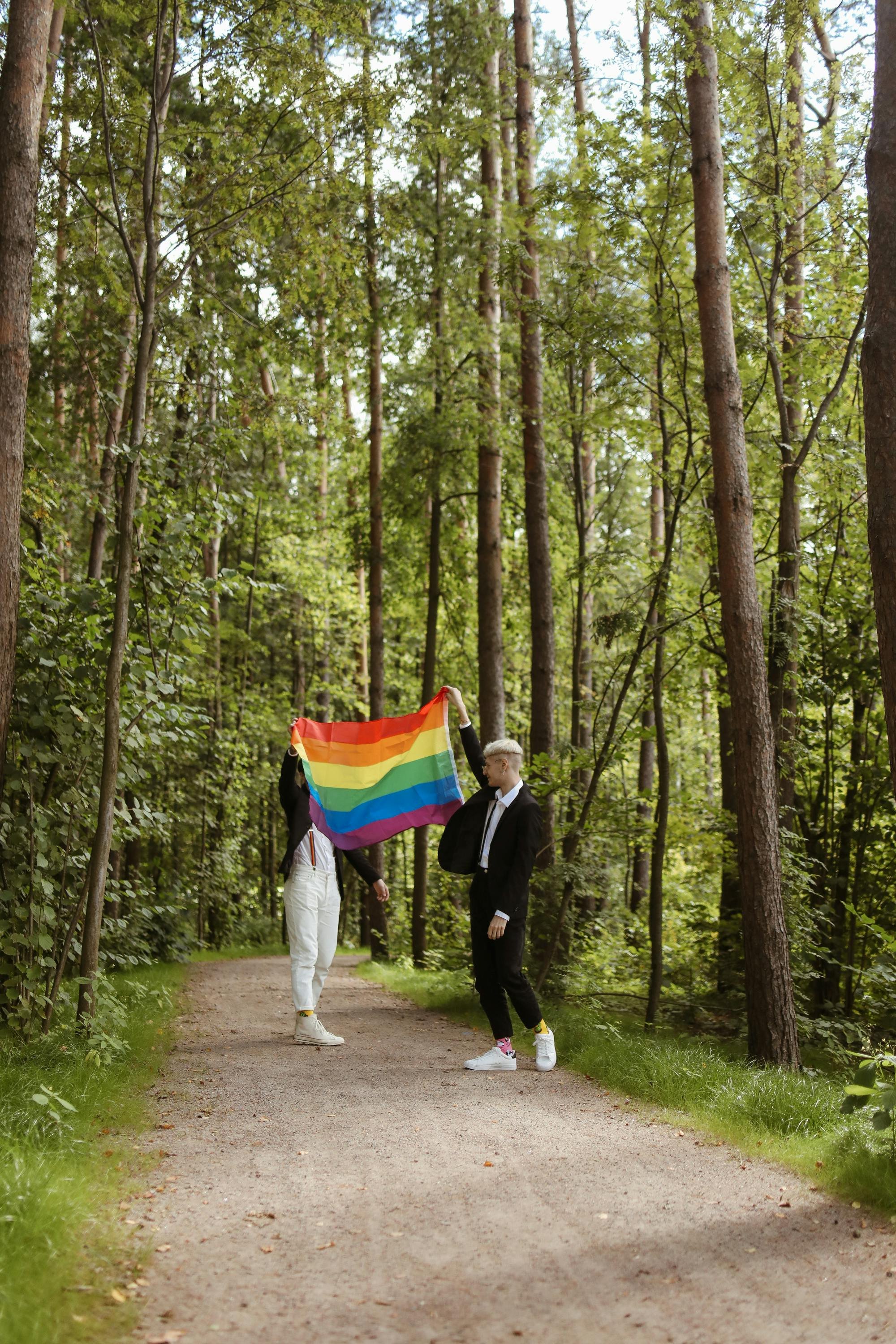 Two men in forest hold up rainbow LGBTQ+ pride flag