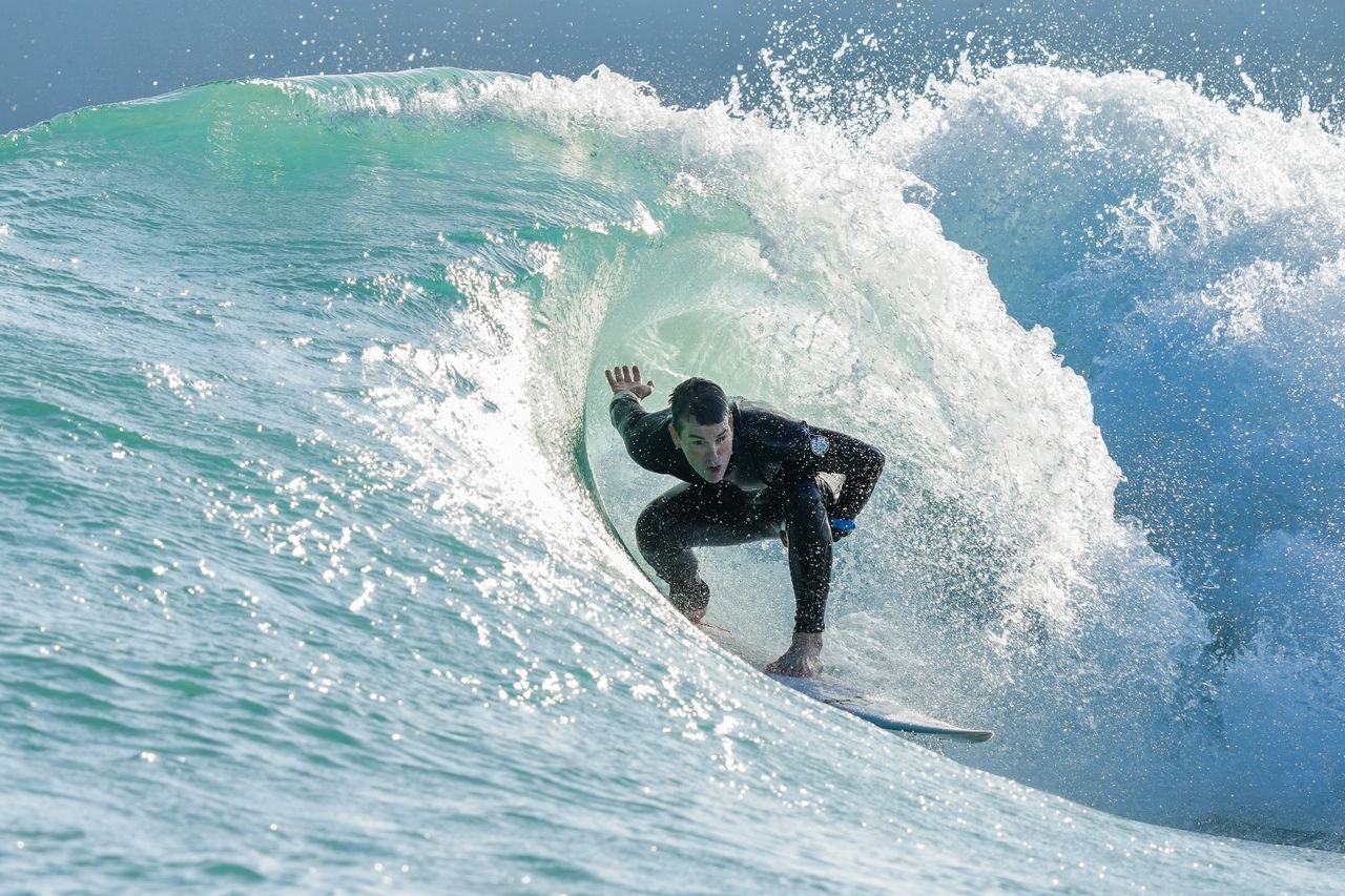 Man in black wetsuit surfing as a wave curls over him, much like how you can surf a wave of anxiety. Photo by Jason Black.